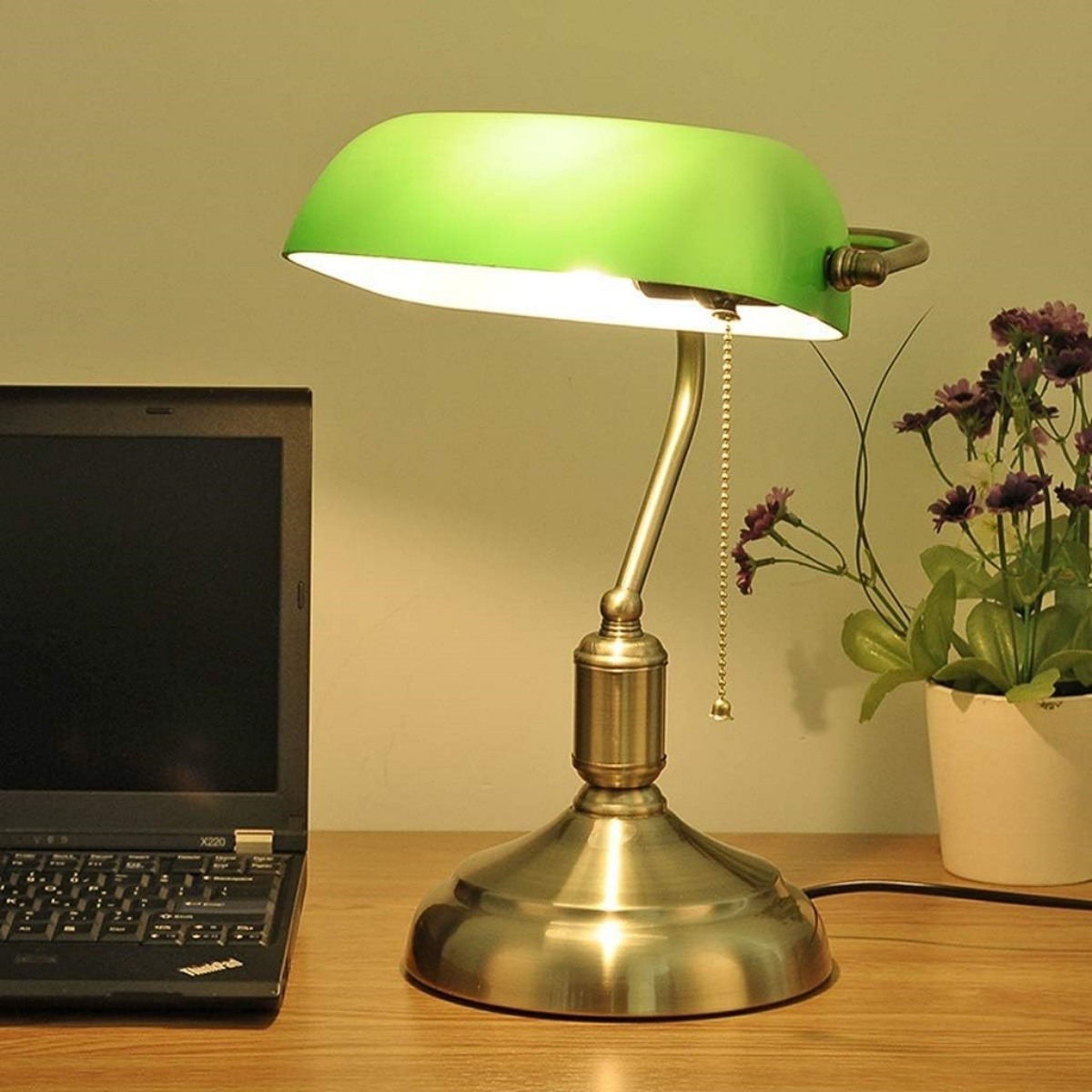 Eine grün schattierte Schreibtischlampe mit goldfarbenem Sockel. Ein schwarzer Laptop steht auf dem Schreibtisch.