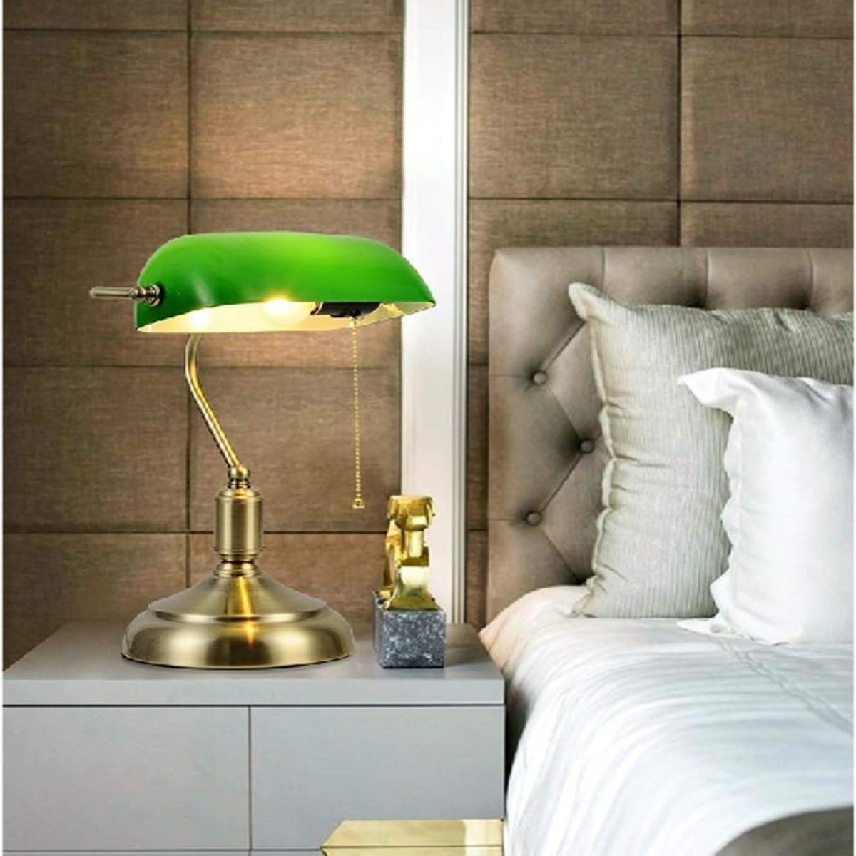Grüner Lampenschirm Schreibtischlampe auf einem Nachttisch. Goldene Basis, weißes Bett und braune Wand.