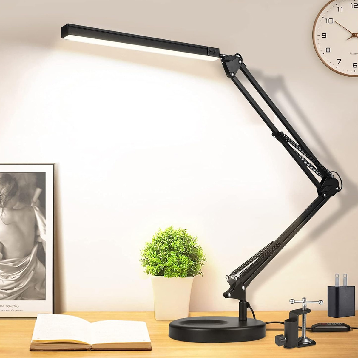 Schwarze, verstellbare Schreibtischlampe auf einem Holztisch mit Bild und Uhr.