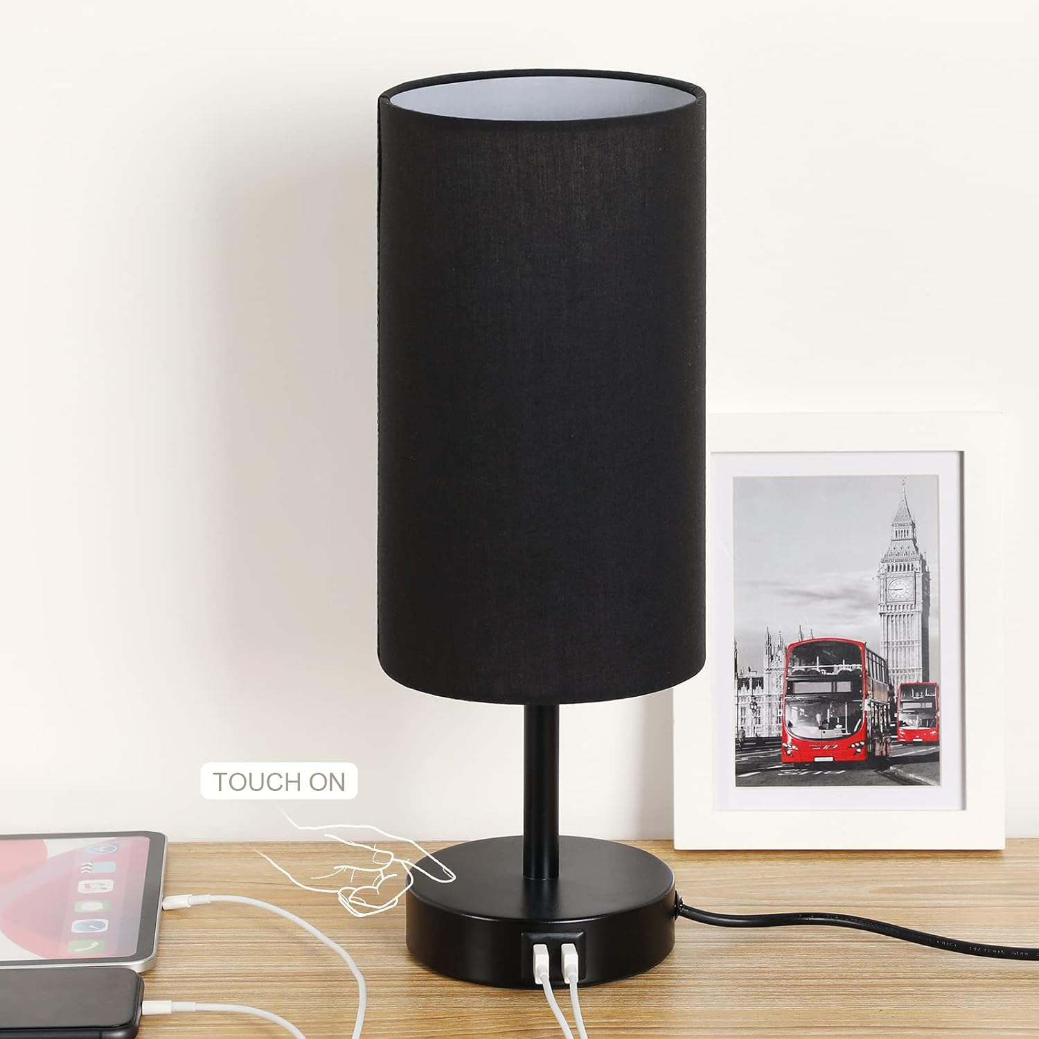 Eine schwarze Tischlampe mit schwarzem Lampenschirm, ein Bild eines Londoner Busses und ein Tablet.