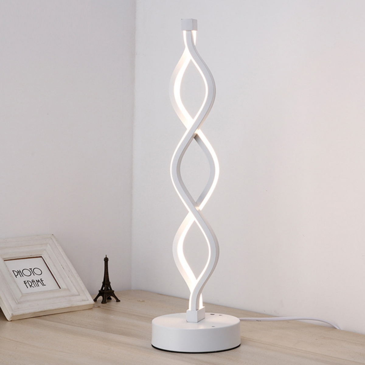 Weiße moderne Lampe mit geschwungenem, verschlungenem Design, auf einem Holztisch. Eiffelturm-Bild.