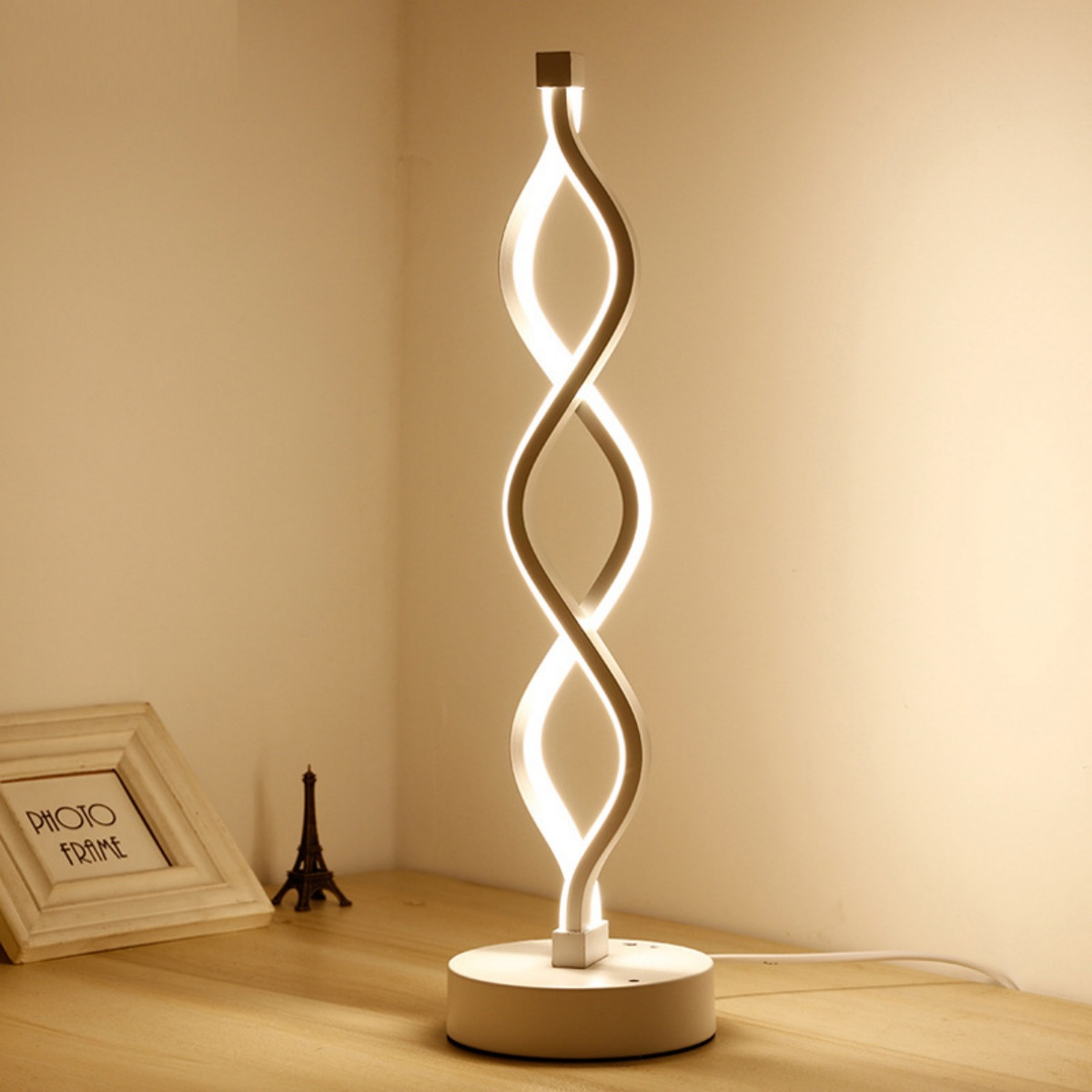 Moderne weiße Tischlampe mit Spiraldesign, neben einem Fotorahmen und einem Miniatur-Eiffelturm.
