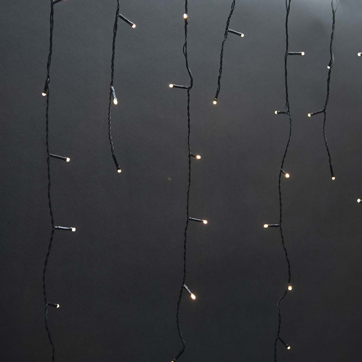 Black string lights with small, bright bulbs, arranged against a dark, gray background.