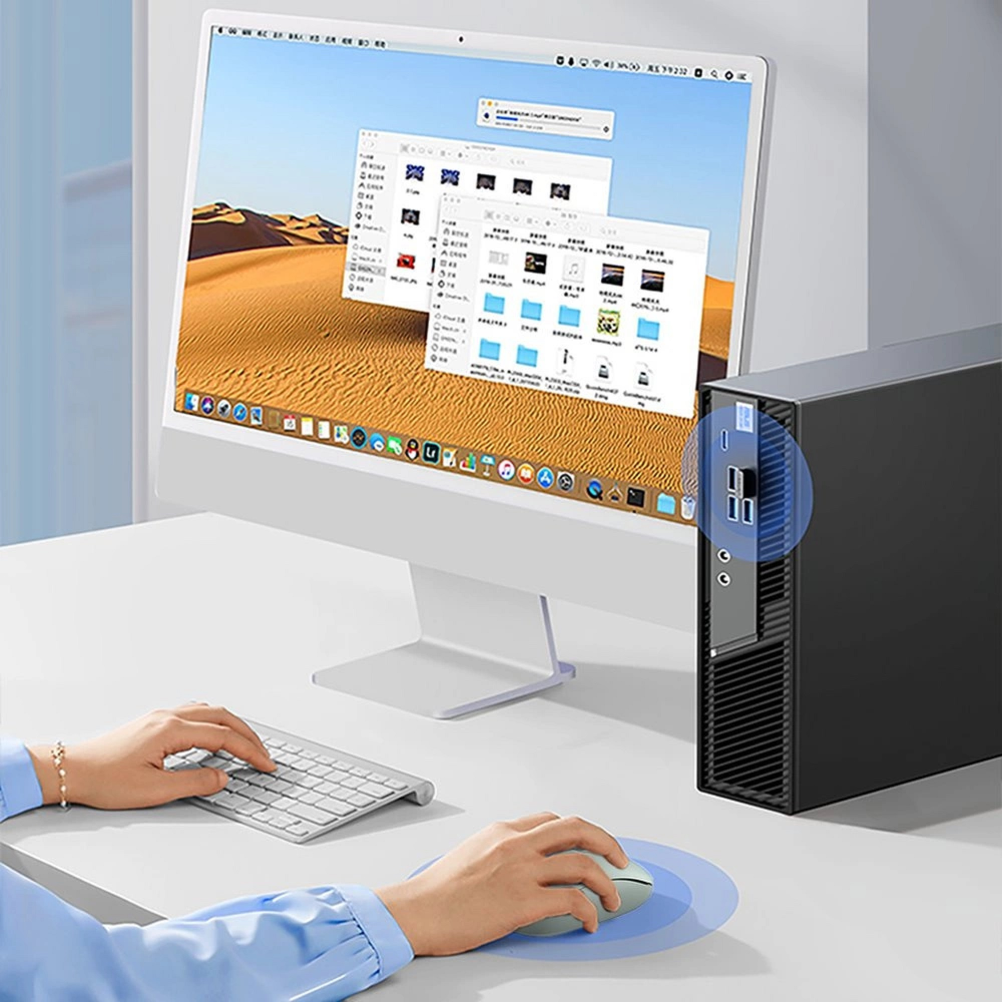 Eine Person, die an einem Computer mit Tastatur und Maus arbeitet. Ein Desktop-Computer befindet sich auf der rechten Seite des Schreibtischs.