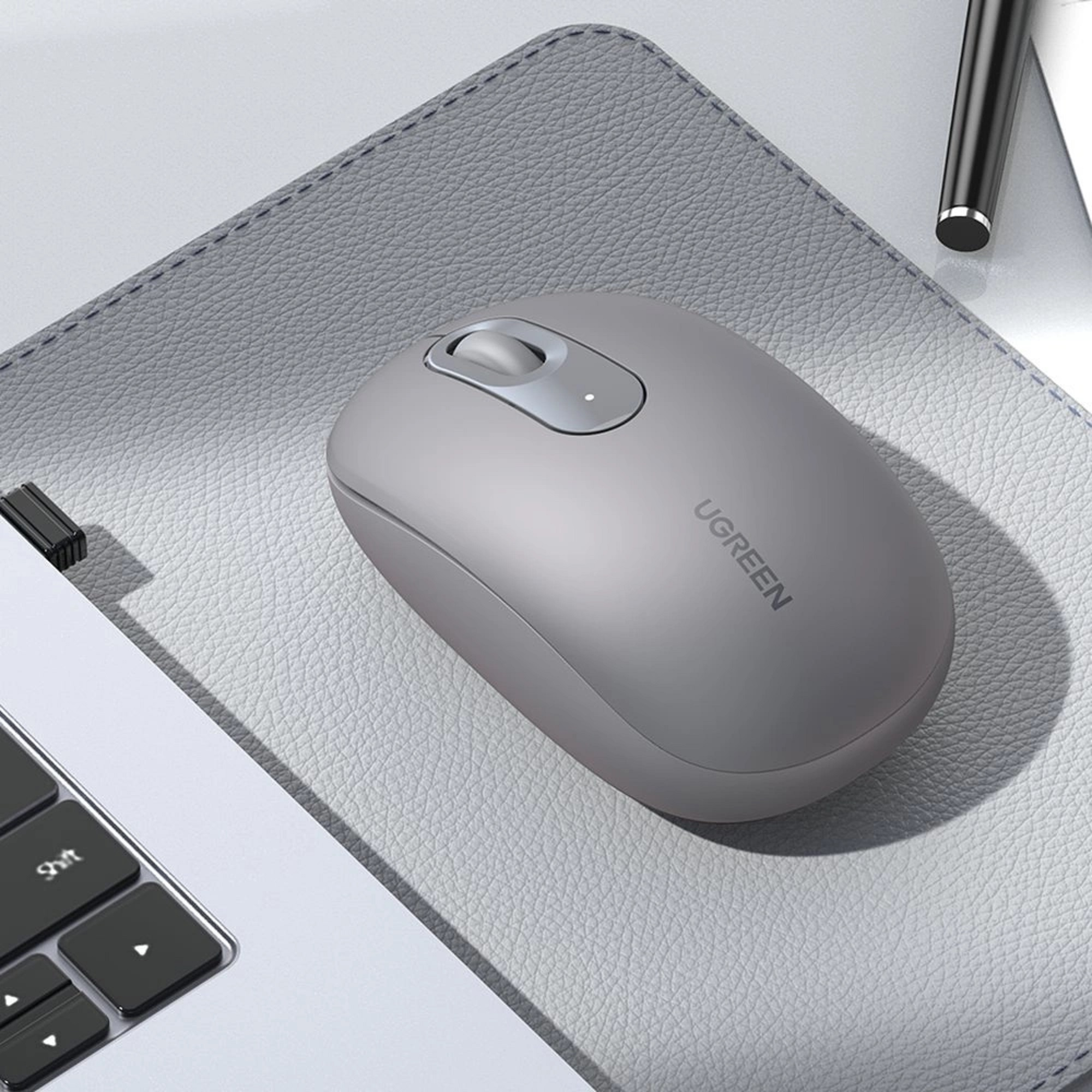 Graue Computermaus auf einem grauen Mauspads, in der Nähe einer Laptop-Tastatur, mit der Marke 'UGREEN'.