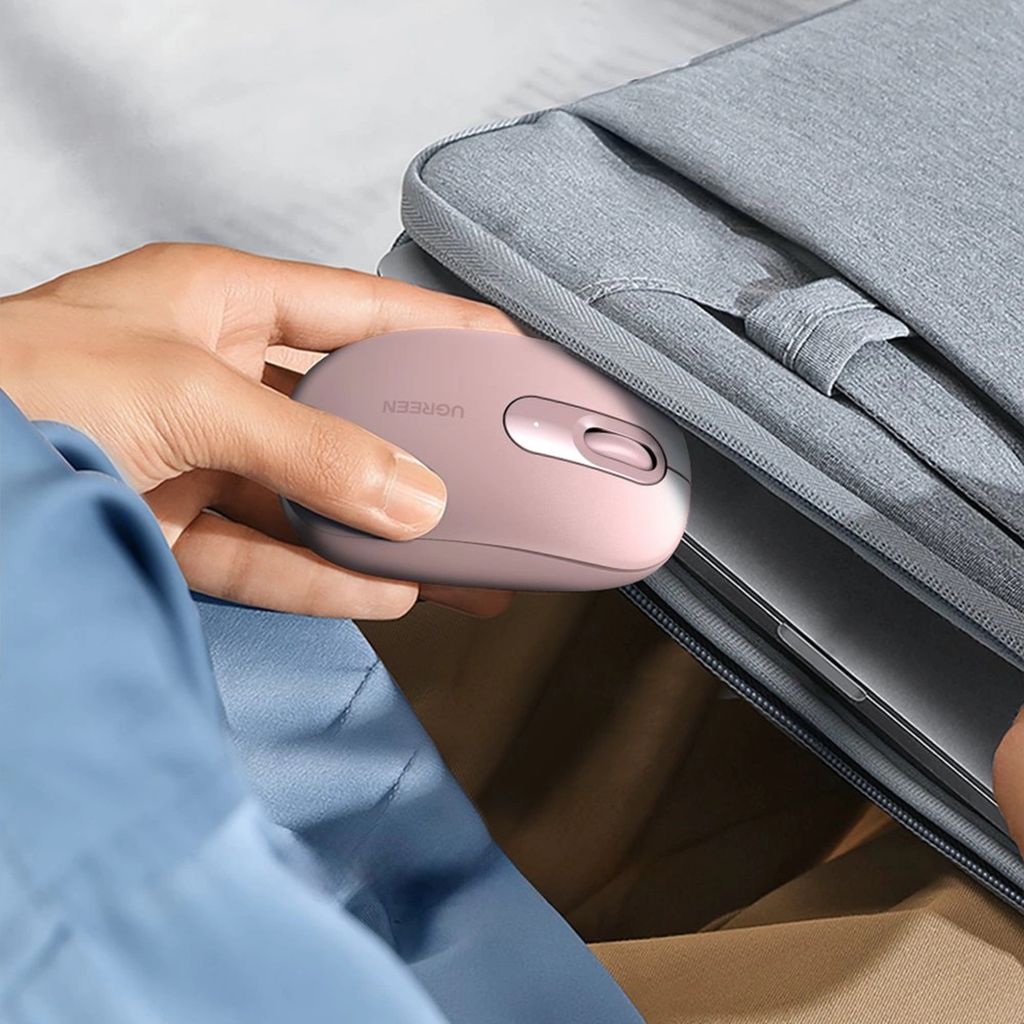 Eine rosa Maus liegt auf einer Tasche neben einem Laptop.