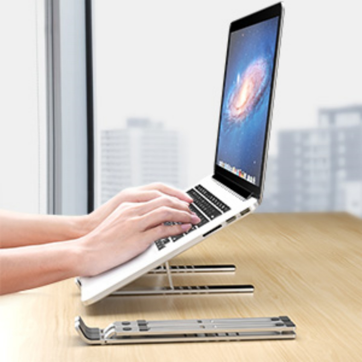 Ein Laptop auf einem silbernen Ständer in Gebrauch. Der Ständer ist zusammenklappbar, der Hintergrund unscharf.
