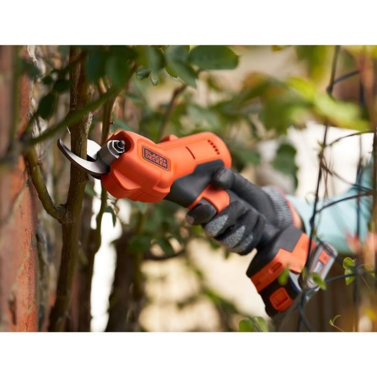 Eine orangefarbene elektrische Heckenschere von BLACK+DECKER schneidet einen Ast. Der Benutzer trägt Handschuhe.