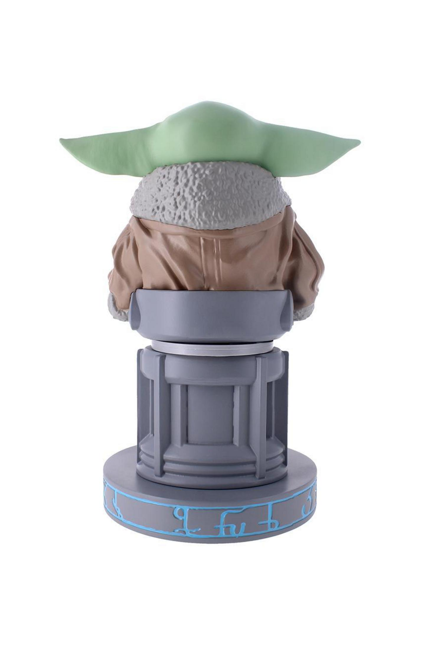 Statuetta di Baby Yoda vista da dietro. Orecchie verdi, cappotto marrone, su base grigia.