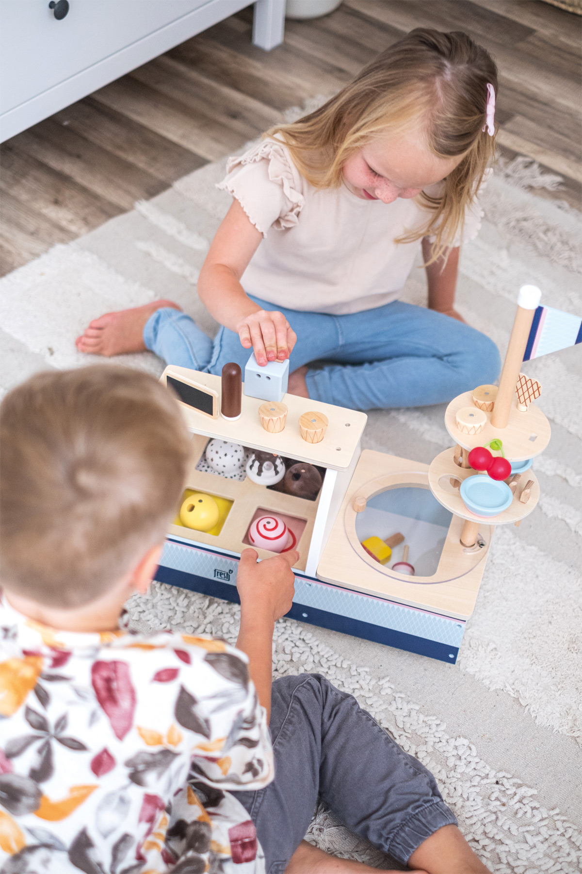 Zwei Kinder spielen mit einem Eisdielen-Spielzeug aus Holz. Ein Kind tätigt einen Einkauf.