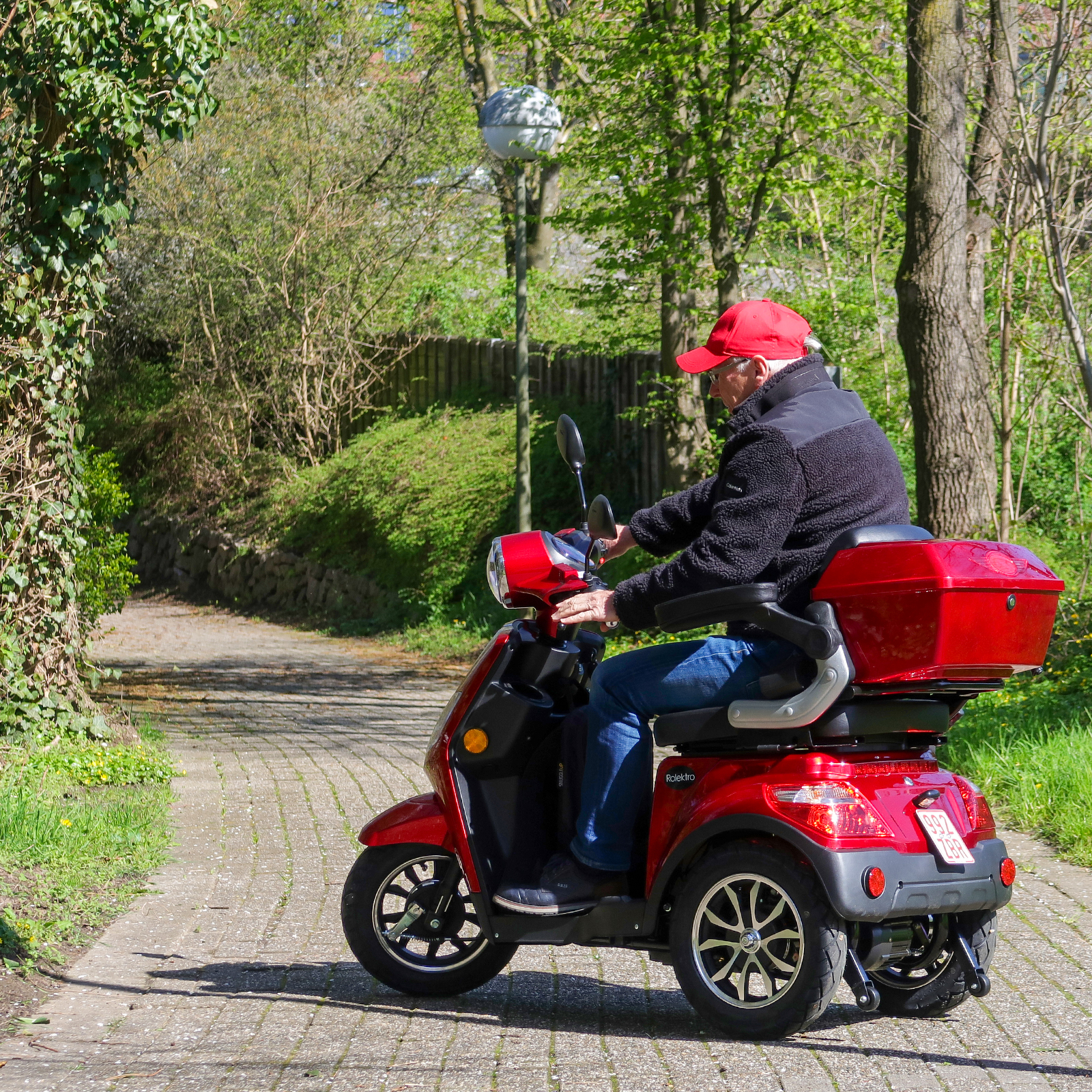 Person fährt roten Mobilitätsroller auf einem gepflasterten Weg im Park.