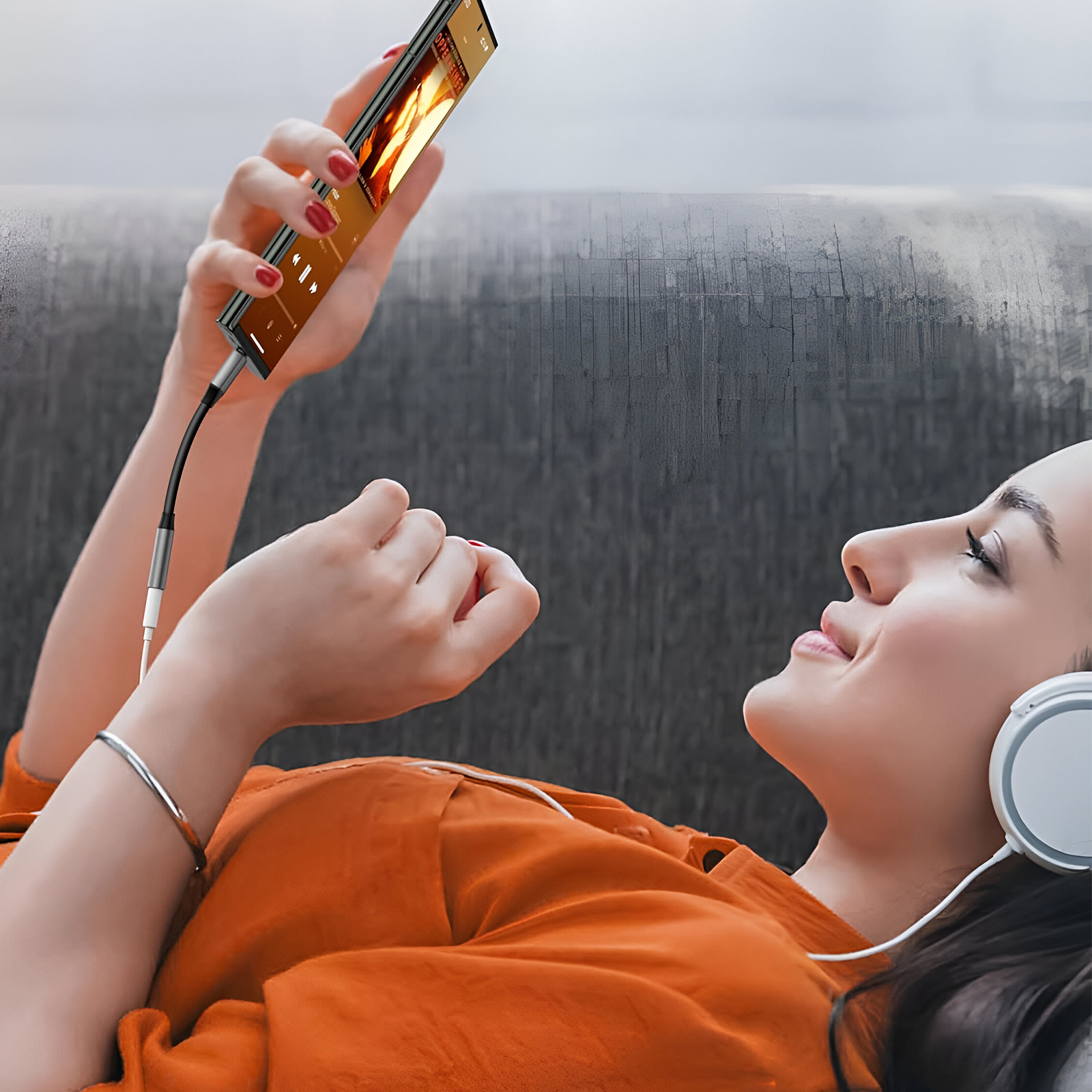 Kobieta leżąca na kanapie słucha muzyki w słuchawkach, używając telefonu.