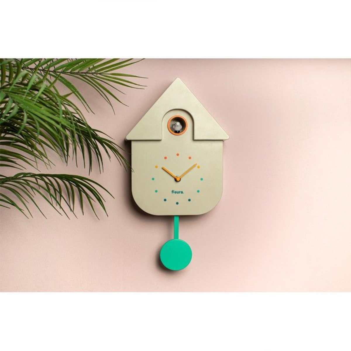 Un orologio a cucù beige, con accenti verdi e arancioni, appeso a una parete rosa.