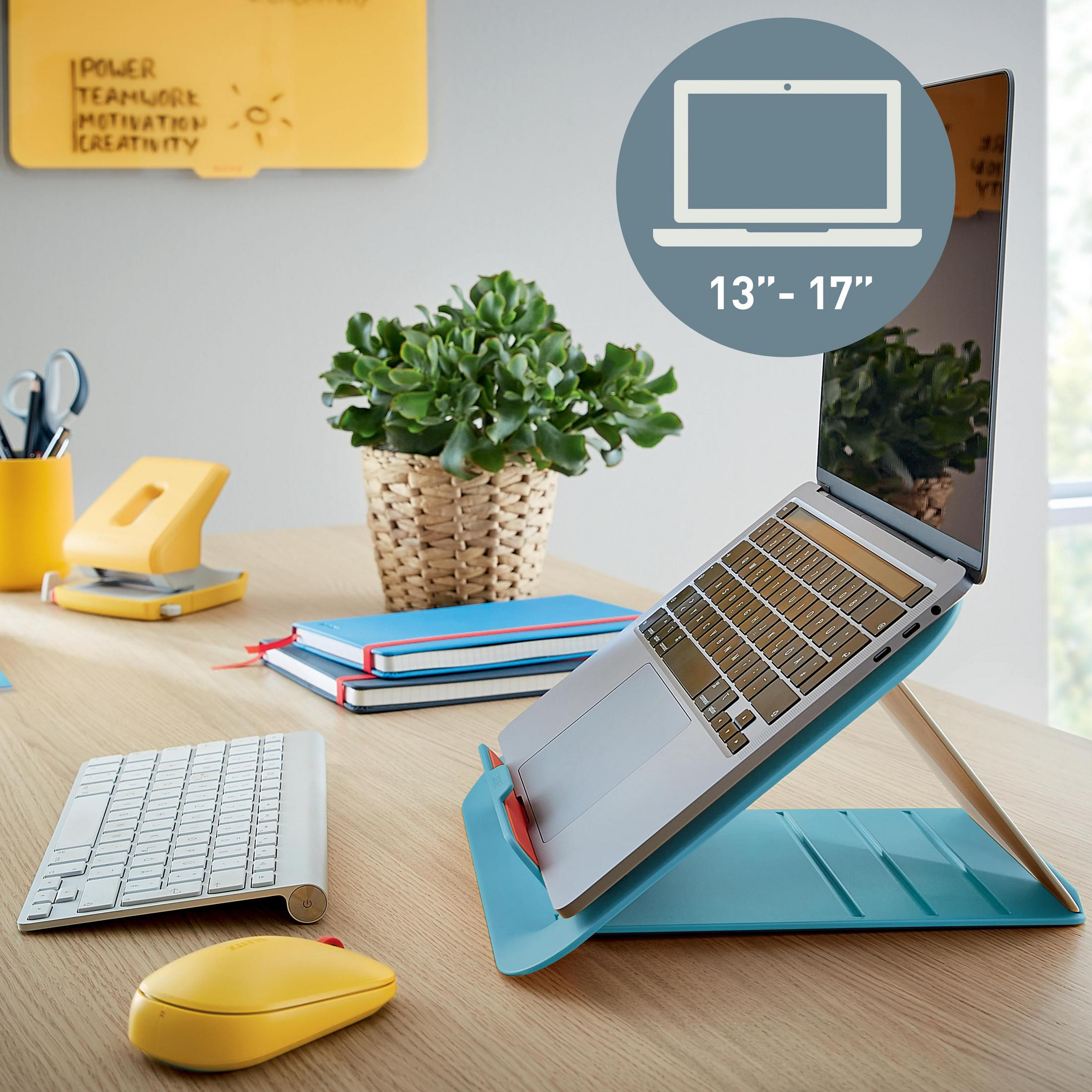 Laptop auf einem blauen Ständer mit Tastatur und Maus, sowie Notizen und einer Pflanze auf dem Schreibtisch.
