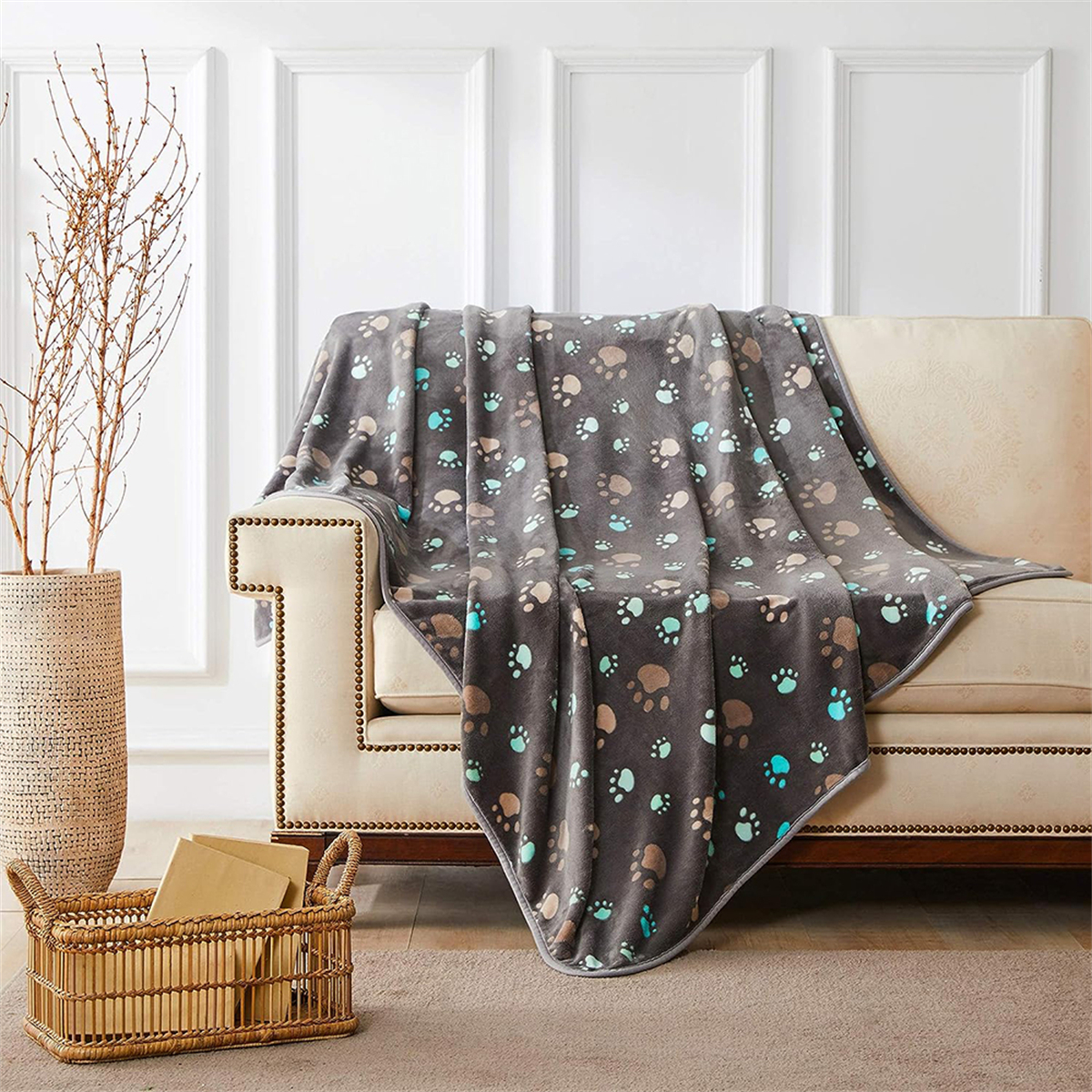 Graue Decke mit Pfotenabdrücken auf einer beigen Couch. Ein Korb und eine Vase befinden sich an den Seiten.
