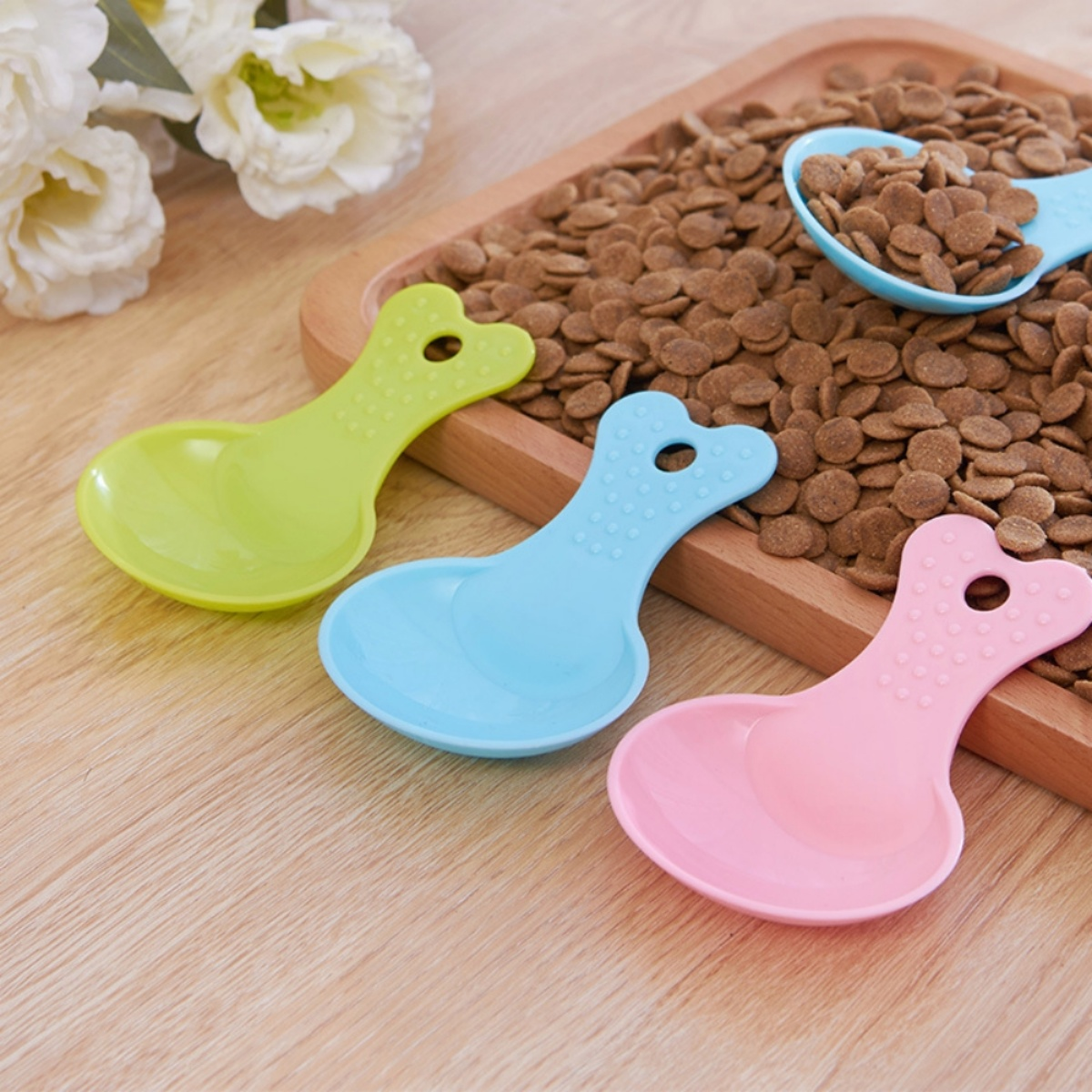 Drei bunte Tierfutterlöffel. Grün, blau und rosa. Braunes Tierfutter und ein Holztablett.