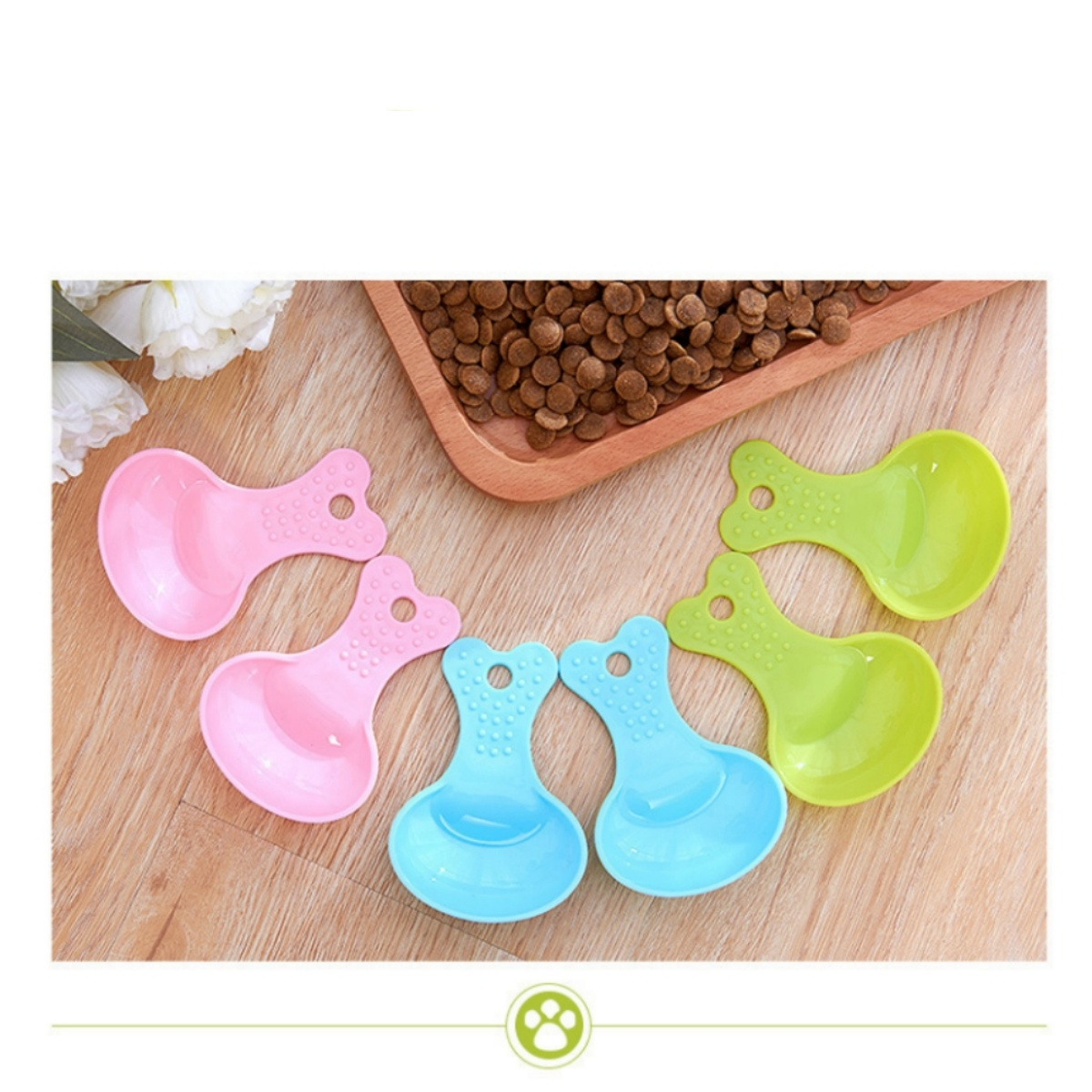Rosa, blaue und grüne Futterschaufeln für Hunde. Sie haben eine Herzform und ein Loch. Sie sind auf einem Holztablett.