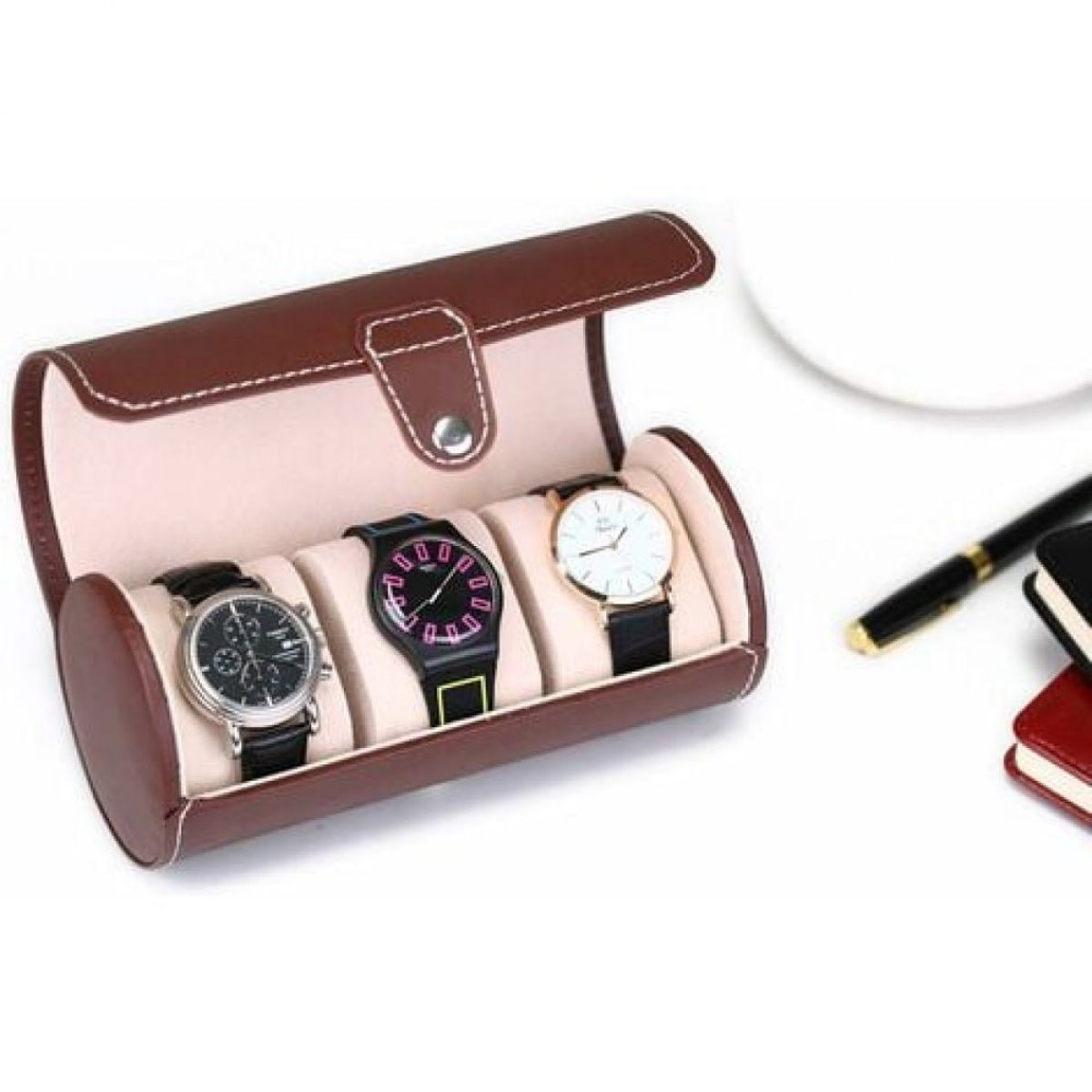 Ein offenes braunes Leder-Uhrenetui zeigt drei Uhren mit schwarzen Armbändern. Ein Stift und ein Notizblock befinden sich rechts.
