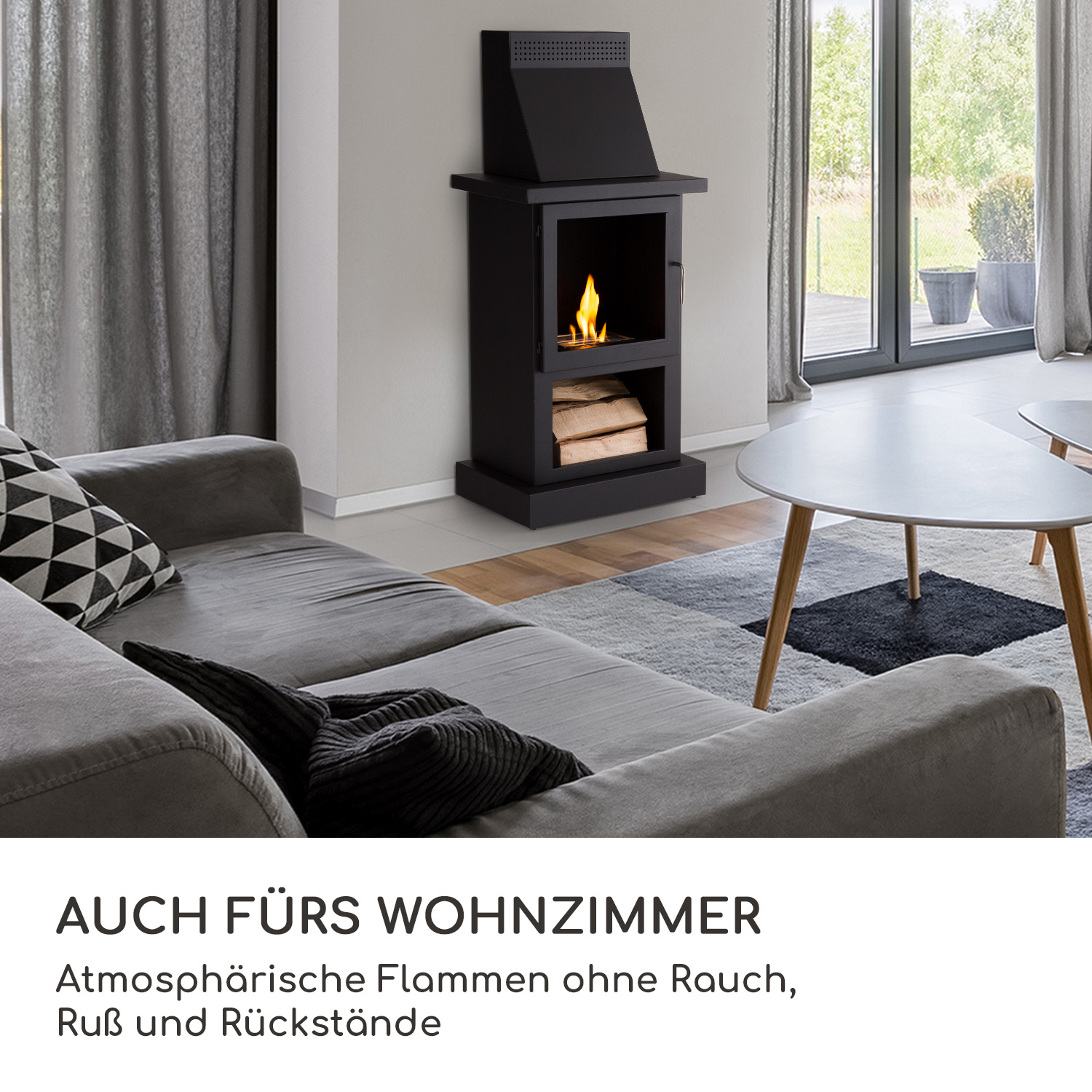 Ein schwarzer Kamin mit Glastür und einem Holzstapel. Er befindet sich in einem Wohnzimmer mit einem grauen Sofa.