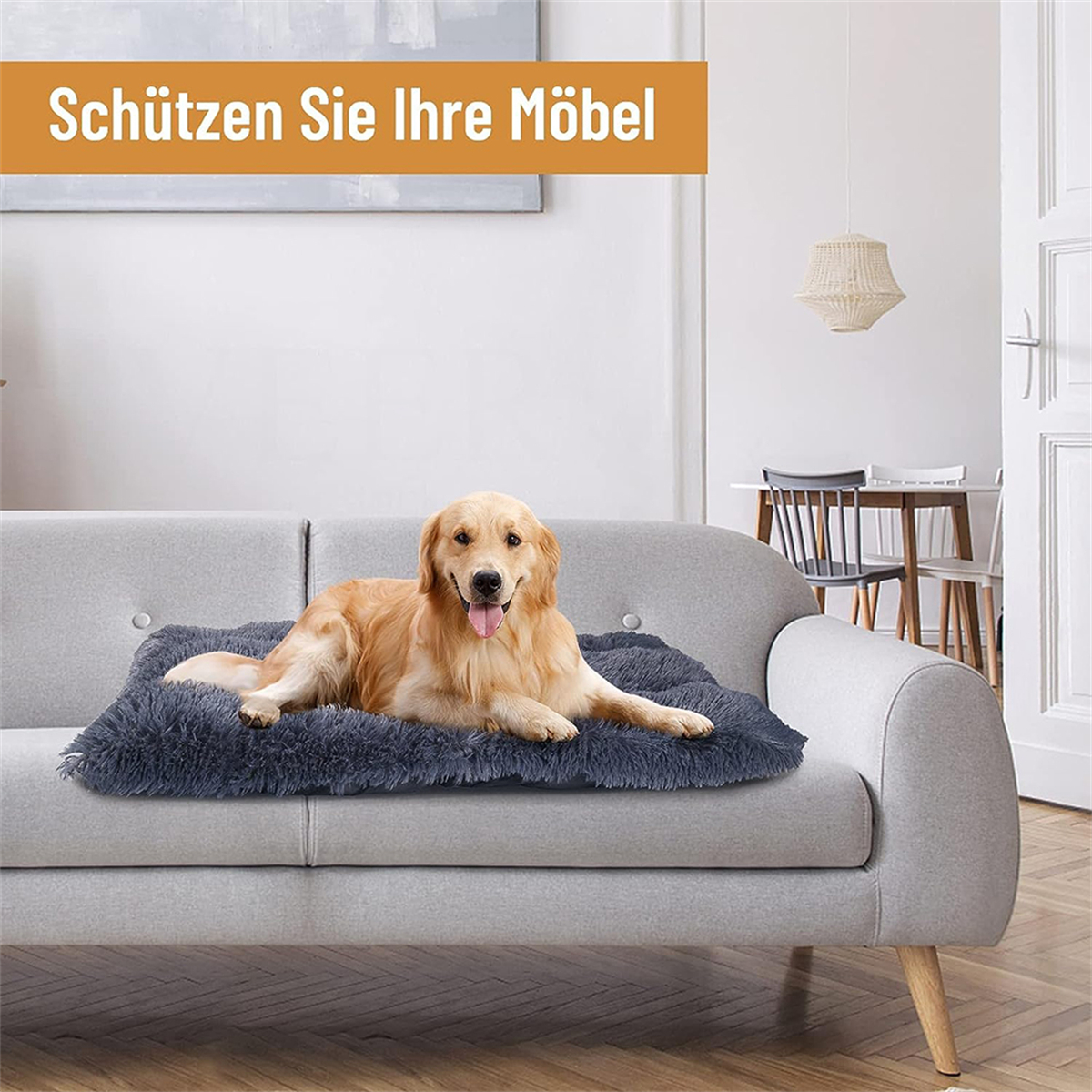 Ein Golden Retriever Hund ruht auf einem flauschigen grauen Hundebett auf einem grauen Sofa.