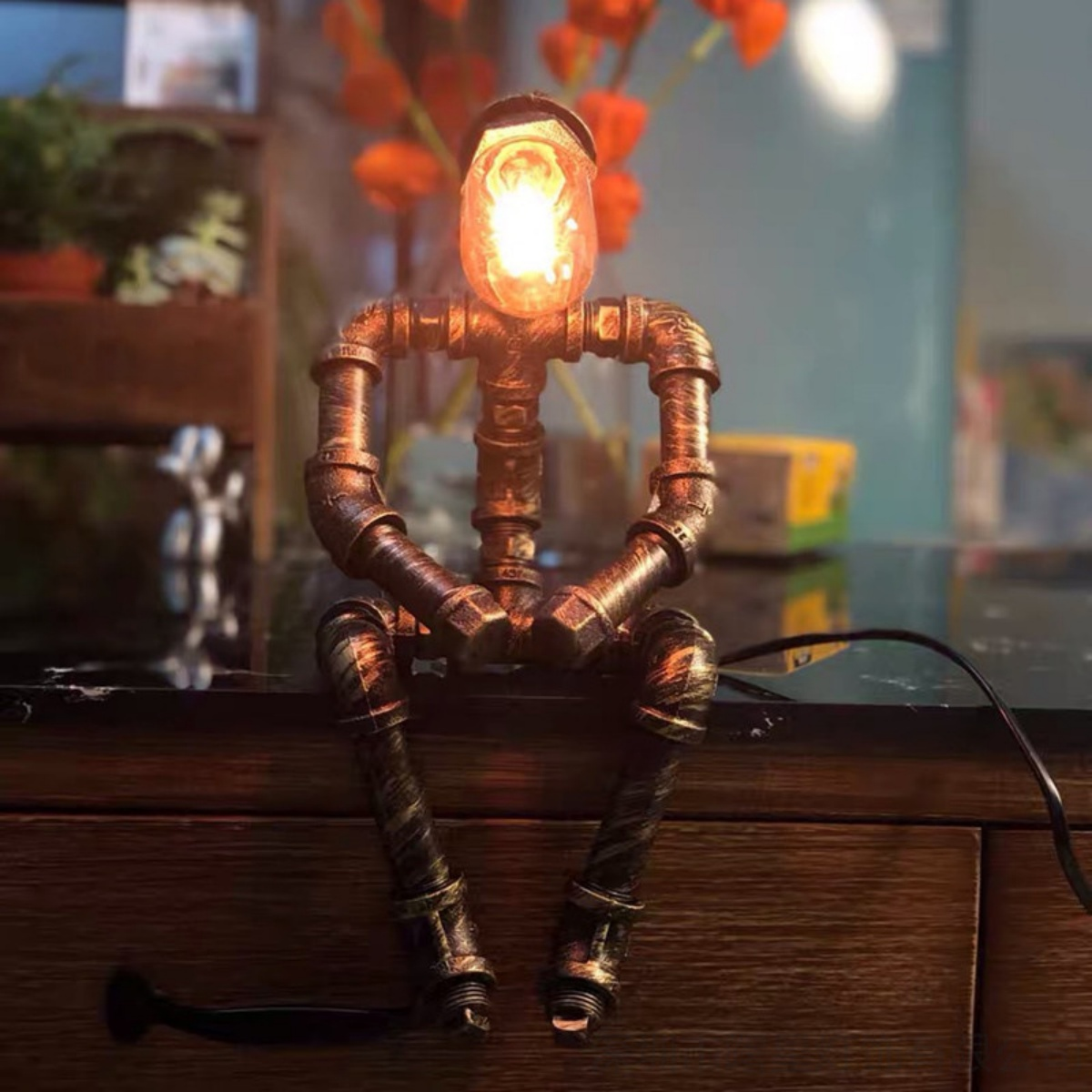 Eine Lampe in Form einer sitzenden Person aus Rohren. Die Glühbirne befindet sich im Kopf.