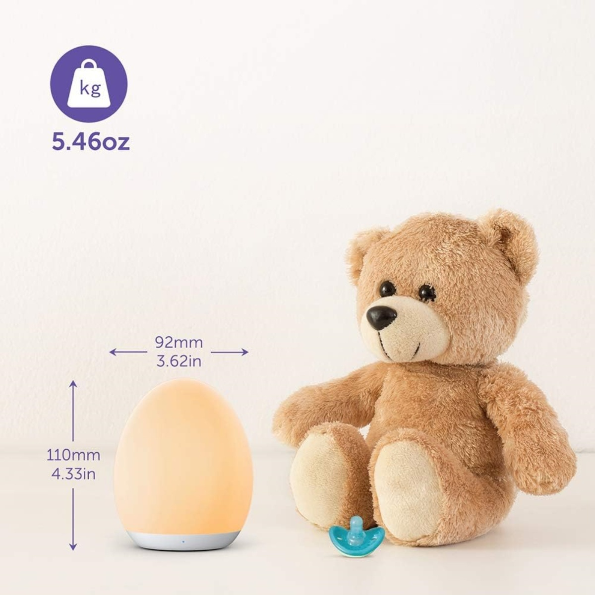 Eine kleine, leuchtende, eiförmige Lampe neben einem Teddybär und einem Schnuller.