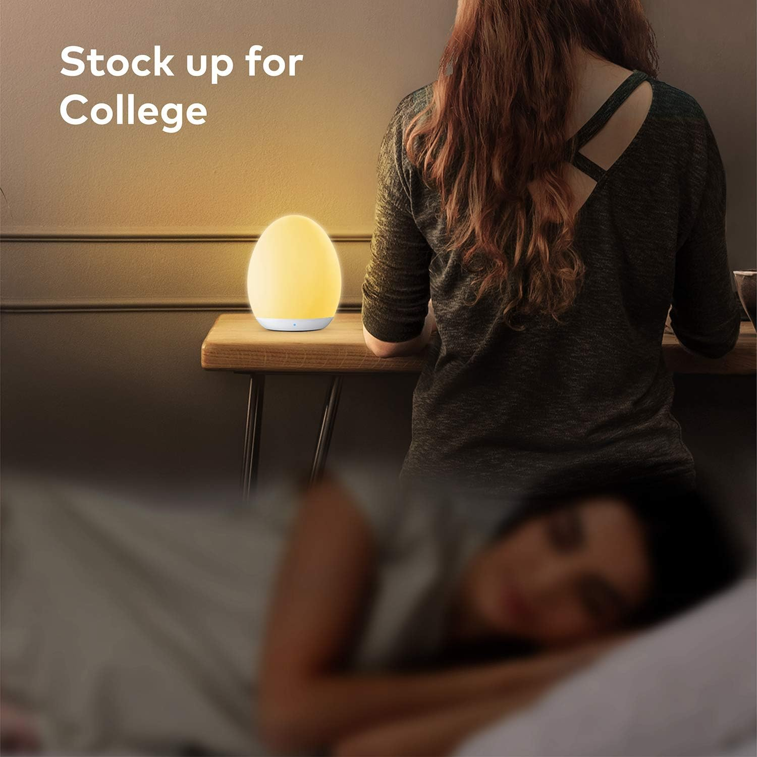 Eine beleuchtete, eiförmige Lampe auf einem Schreibtisch. Eine Person sitzt am Schreibtisch.