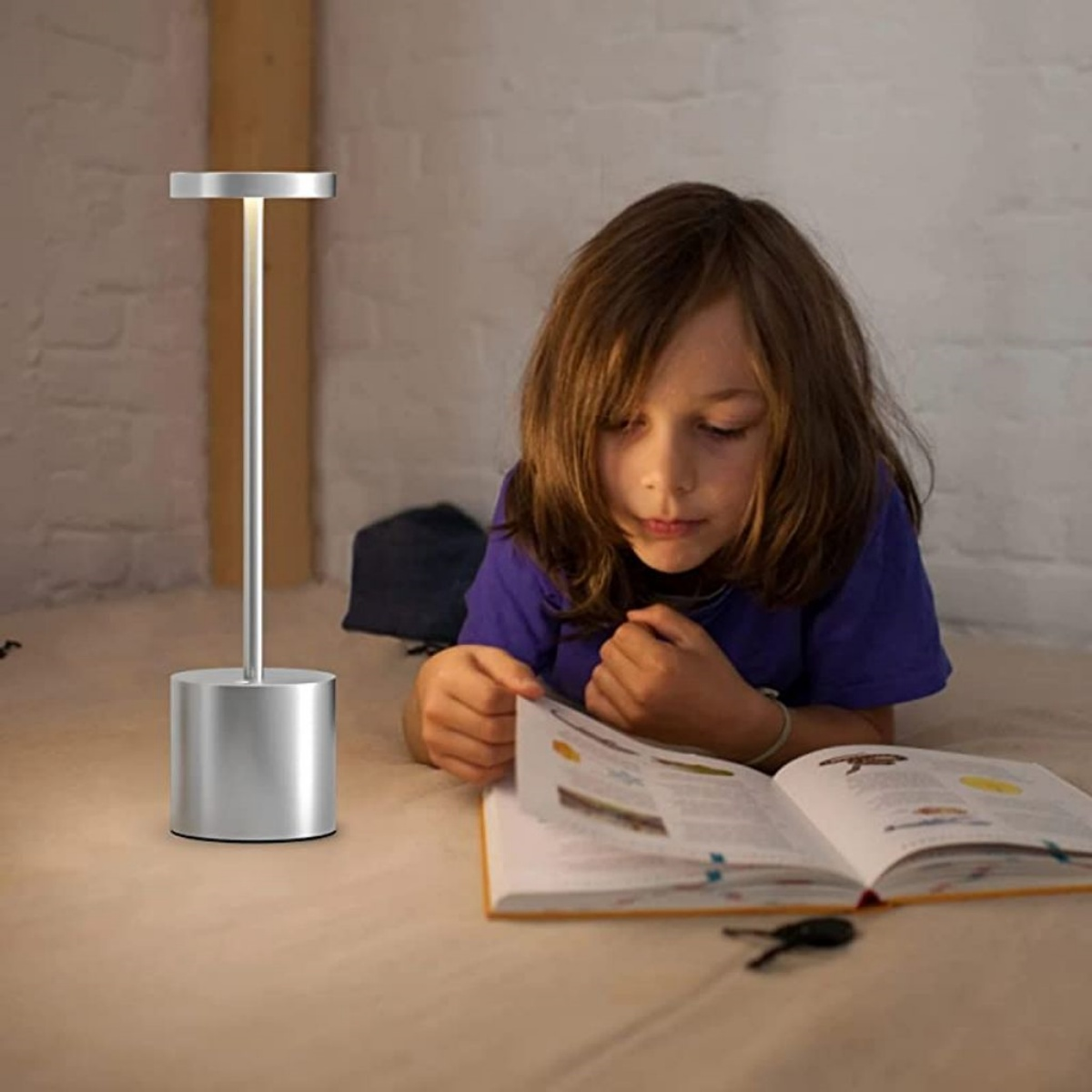 Eine silberne, moderne Lampe auf einem Tisch, mit einem Kind, das ein Buch liest, und einem Schlüssel.