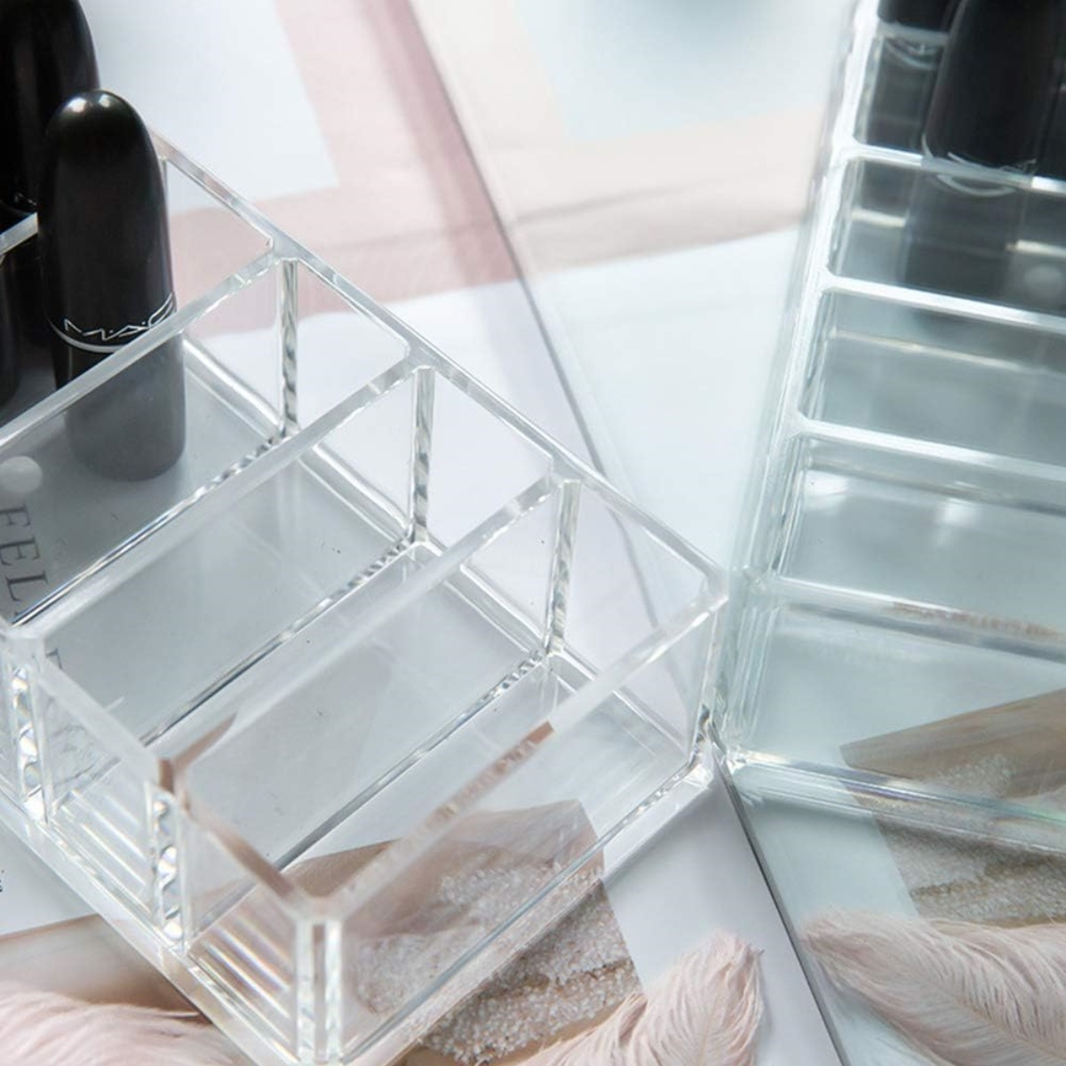 Transparente Lippenstift-Organizer aus Acryl. Sie sind rechteckig, unterteilt und liegen auf einer Oberfläche.