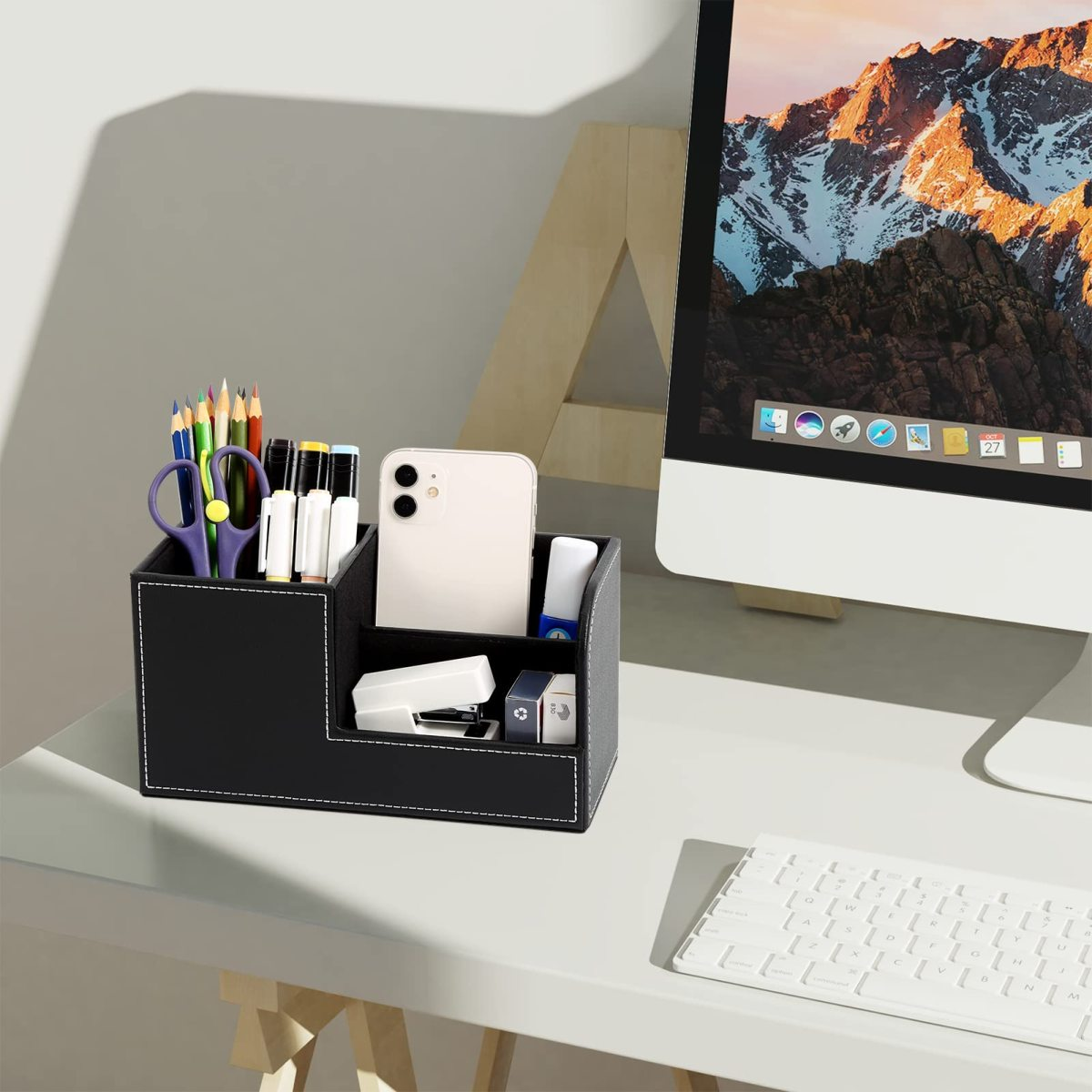 Ein schwarzer Schreibtisch-Organizer mit Stiften, einem Telefon und einem Computer mit weißer Tastatur.