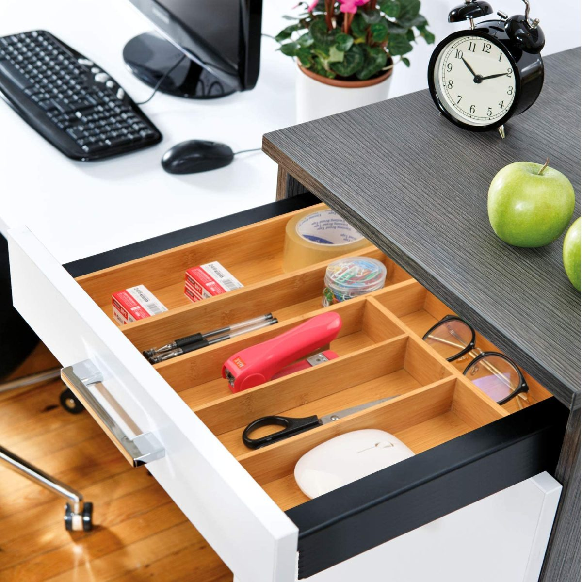 Eine offene Schublade mit Bürobedarf: Hefter, Stifte, Büroklammern und eine Uhr.