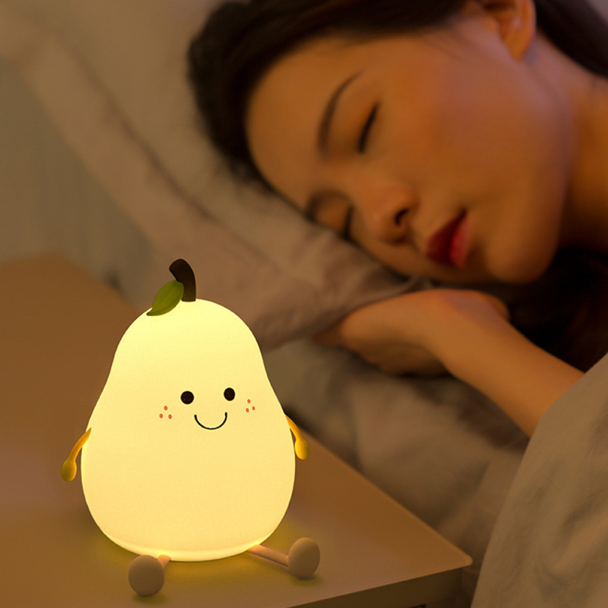 Birnenförmiges Nachtlicht mit lächelndem Gesicht neben einer schlafenden Person im Bett.