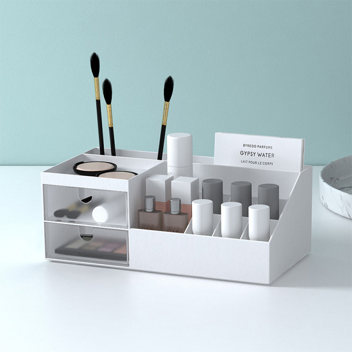 Weißer Kosmetik-Organizer mit Make-up-Pinseln, Produkten und einer kleinen Schublade. Der Hintergrund ist hellblau.
