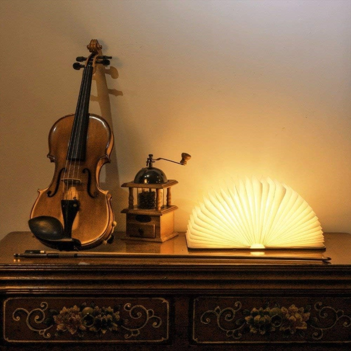Geige, Kaffeemühle und buchförmiges Licht auf einem Holztisch. Warme Beleuchtung und dunkler Hintergrund.