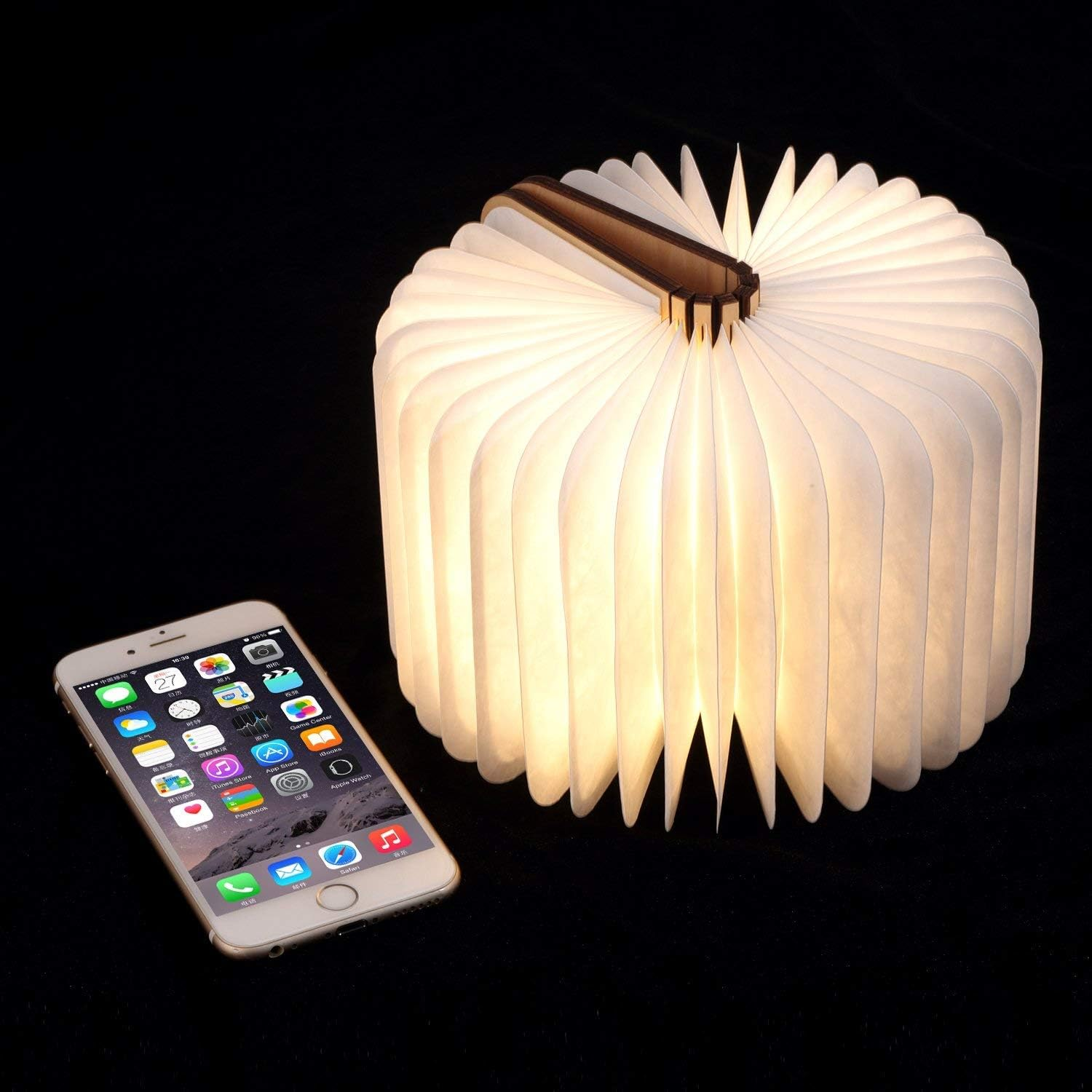 Eine buchförmige Lampe mit beleuchteten offenen Seiten und ein Smartphone daneben.