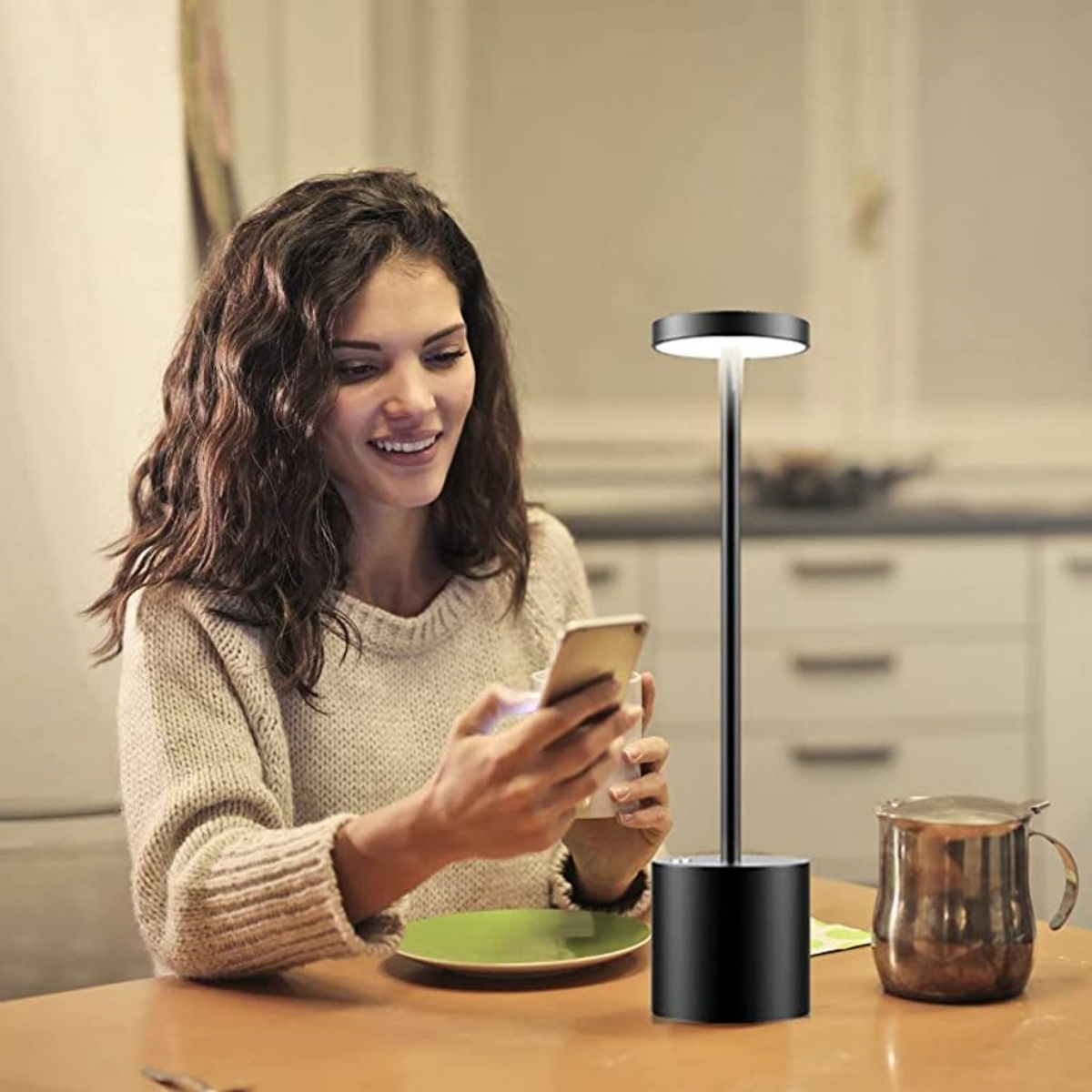 Eine Frau lächelt, während sie ein Smartphone benutzt, mit einer Lampe und Küche im Hintergrund.