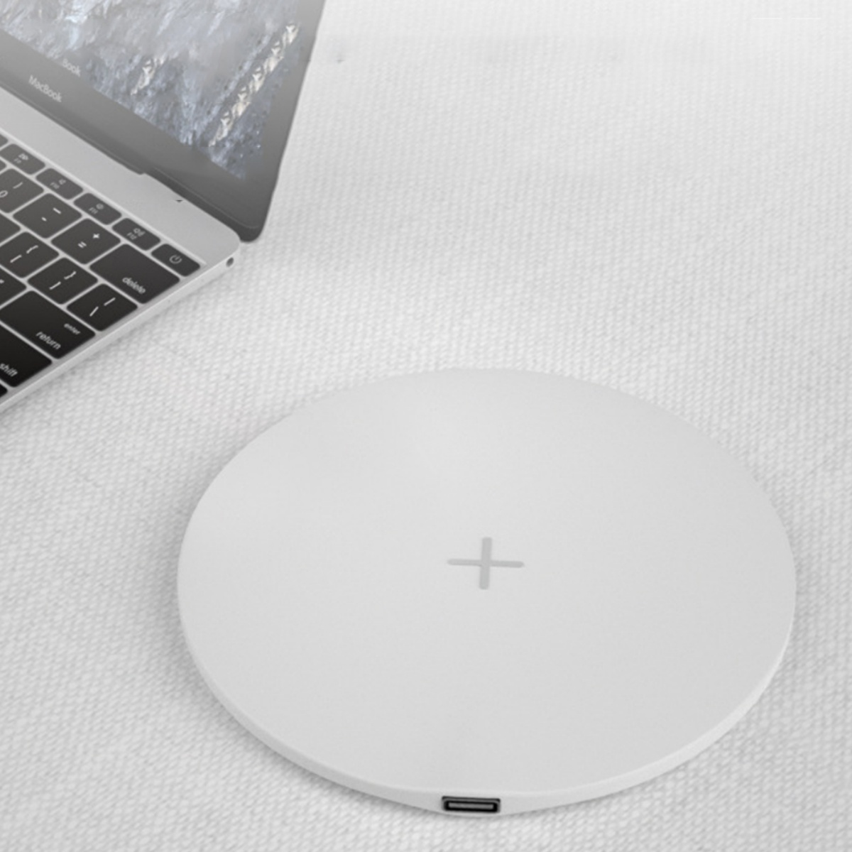 Weißes kabelloses Ladepad mit Plus-Symbol. Ein Laptop ist im Hintergrund.