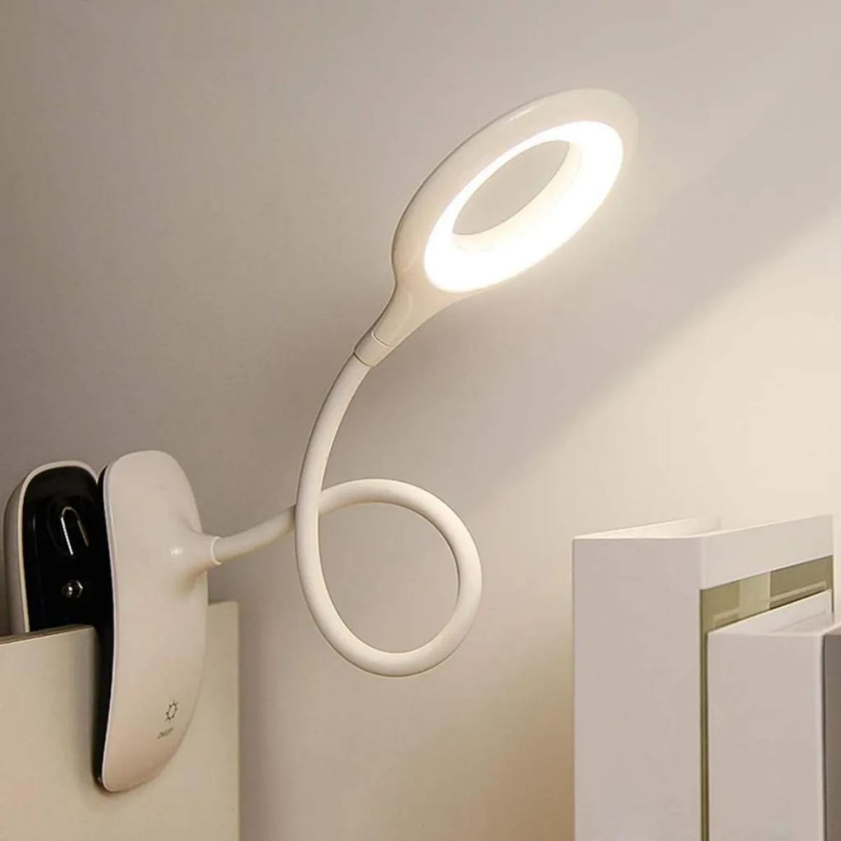 Weiße Schreibtischlampe mit flexiblem Hals, beleuchtet eine weiße Oberfläche. Lampe an Clip befestigt.