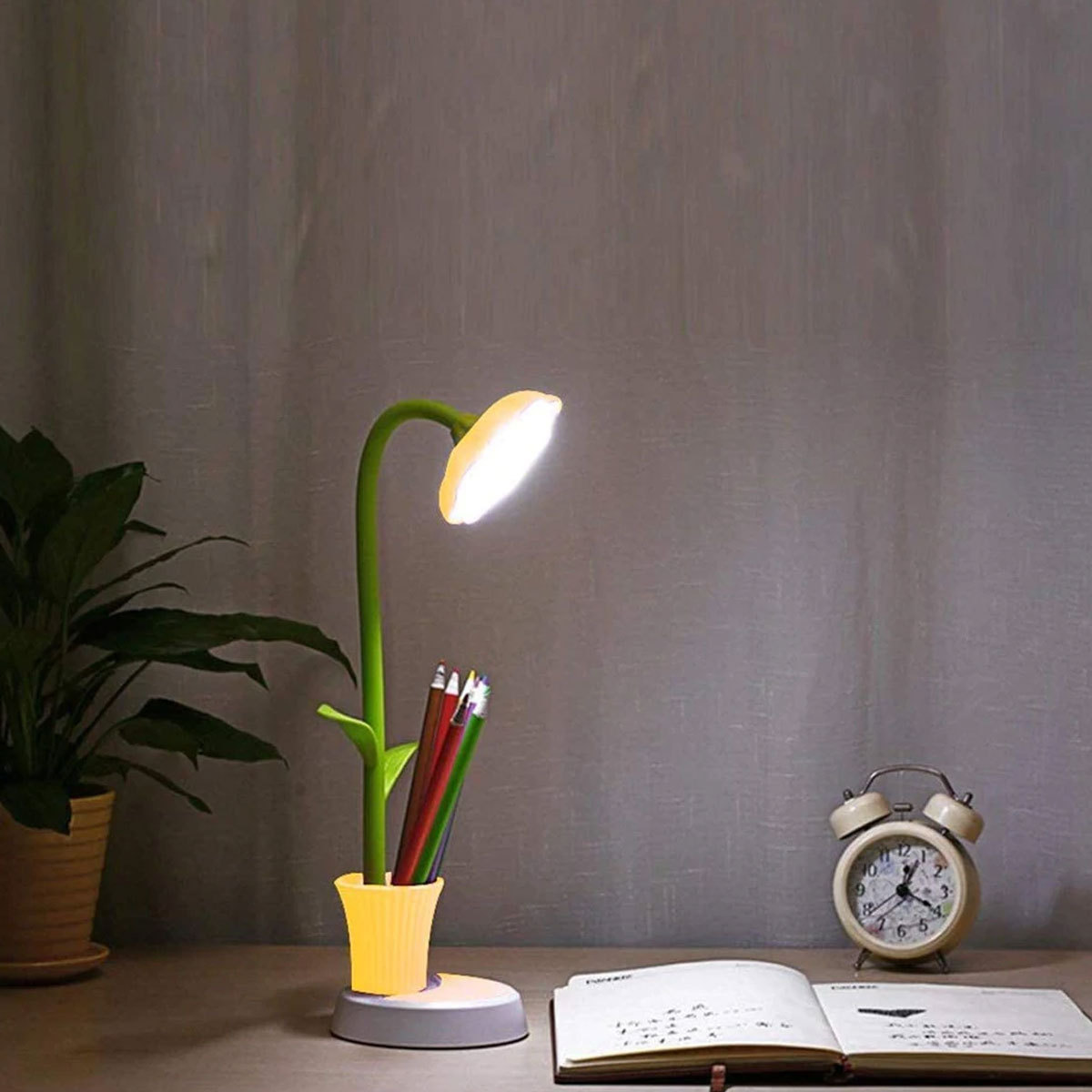 Schreibtischlampe mit blütenförmigem Kopf, grünem Stiel und Stifthalter. Dunkler Hintergrund.