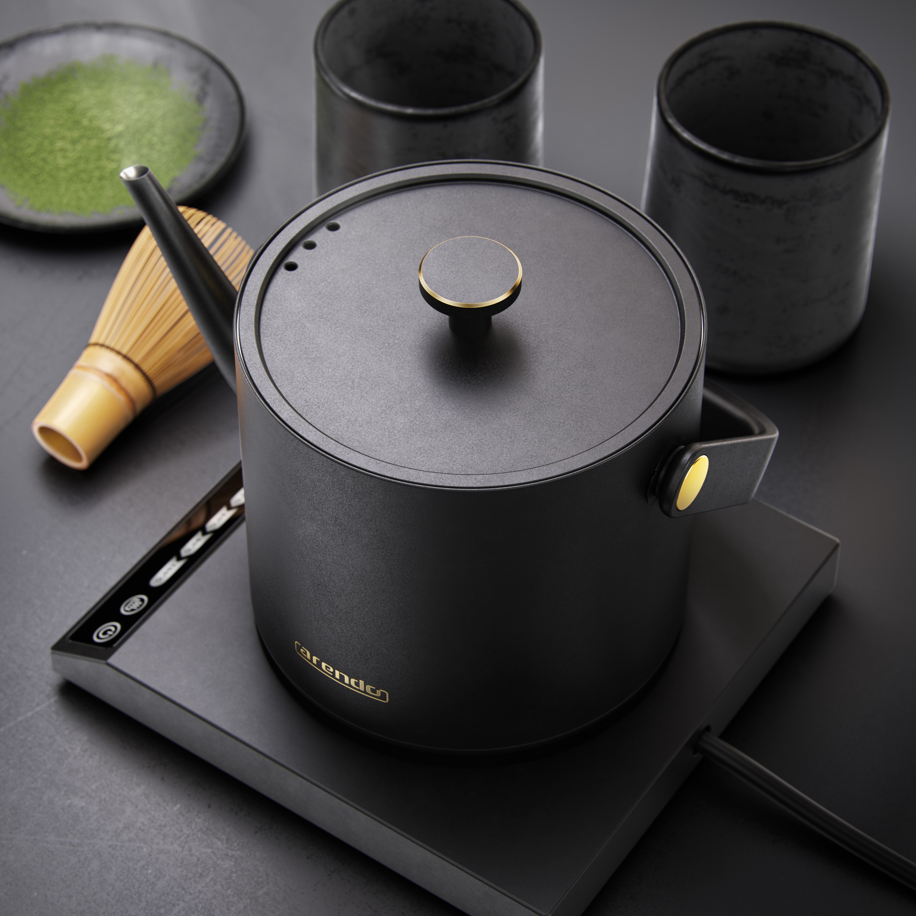 Ein schwarzer Wasserkocher auf einer schwarzen Induktionsbasis, mit einem Matcha-Set im Hintergrund.