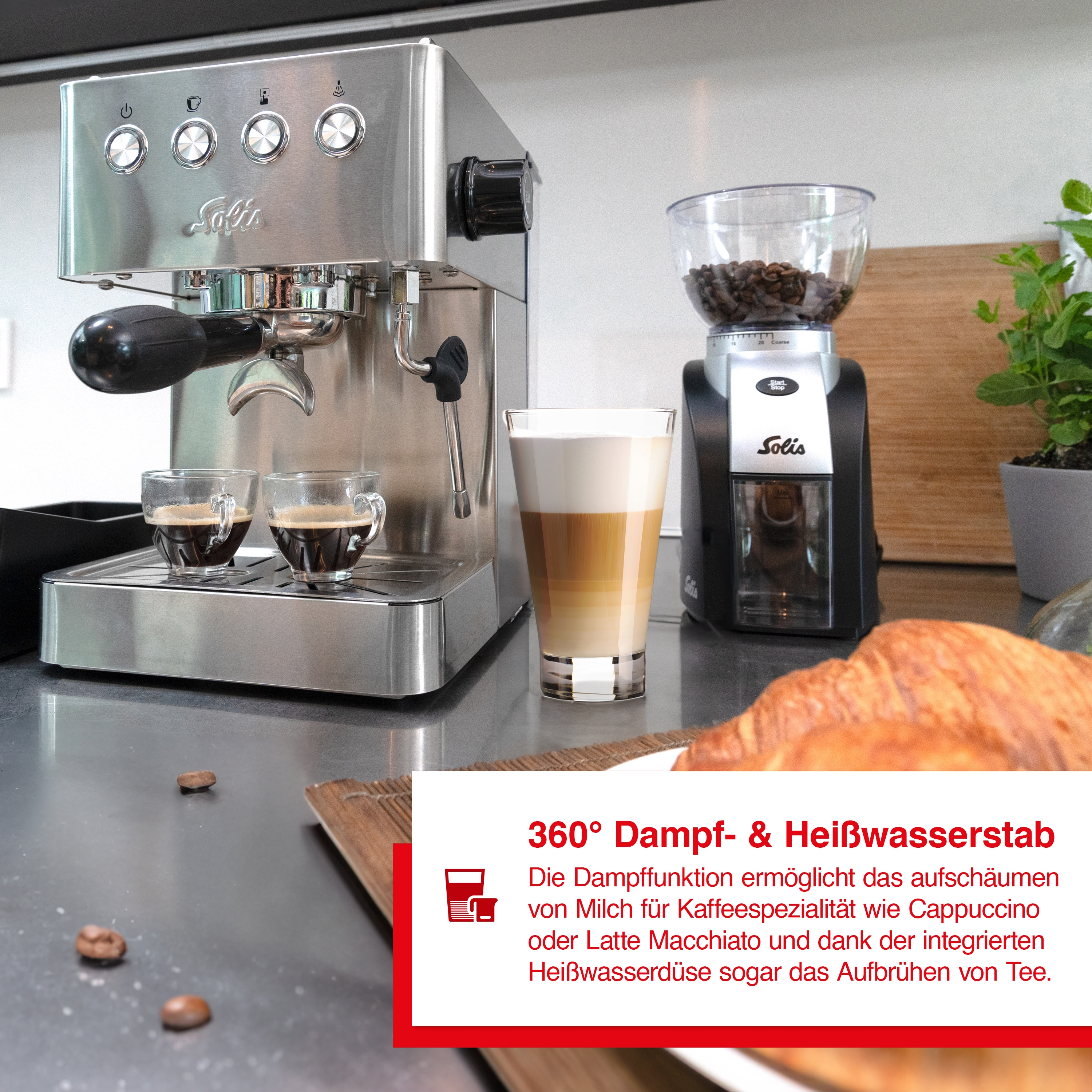 Espressomaschine und Kaffeemühle mit Kaffeetassen und einem Croissant auf einem Tisch.
