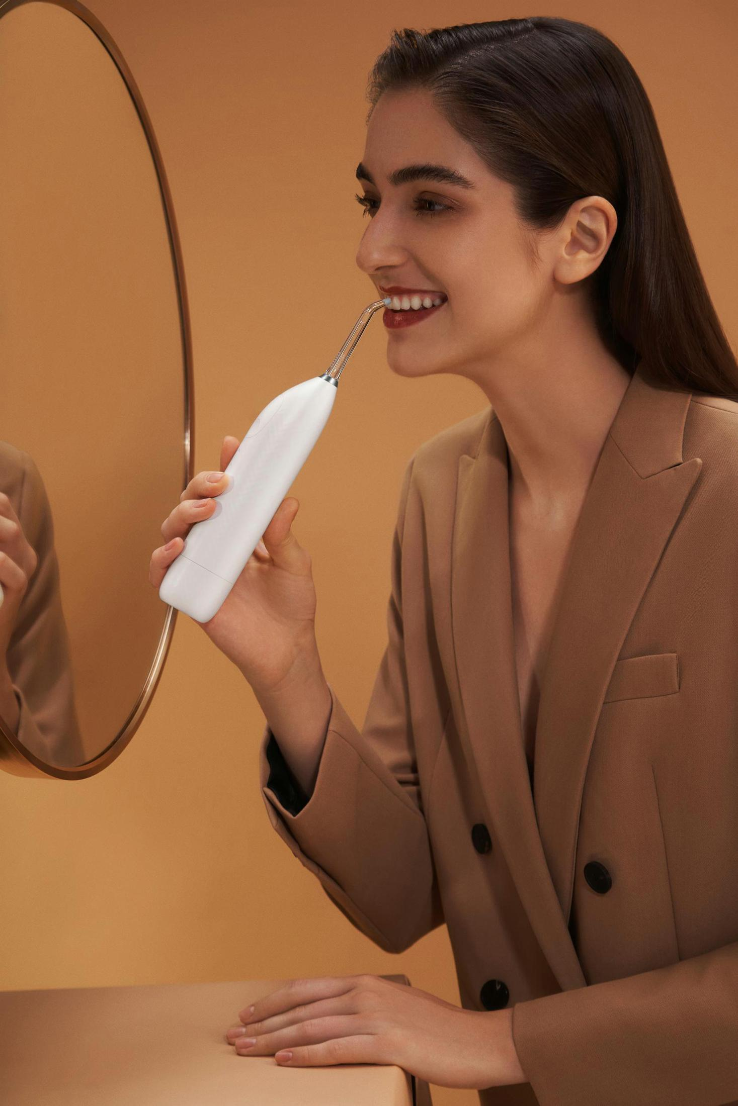 Kobieta używająca białego irygatora do jamy ustnej, uśmiechnięta przed lustrem w łazience.