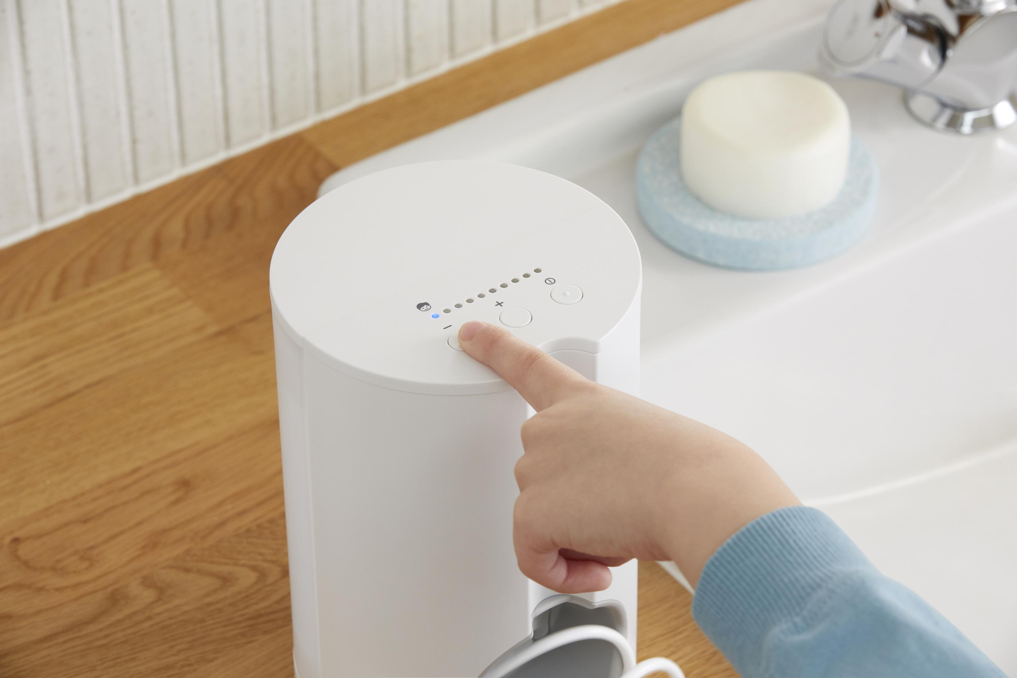 Finger berührt weißes Gerät mit Knöpfen, neben Waschbecken mit Seife.