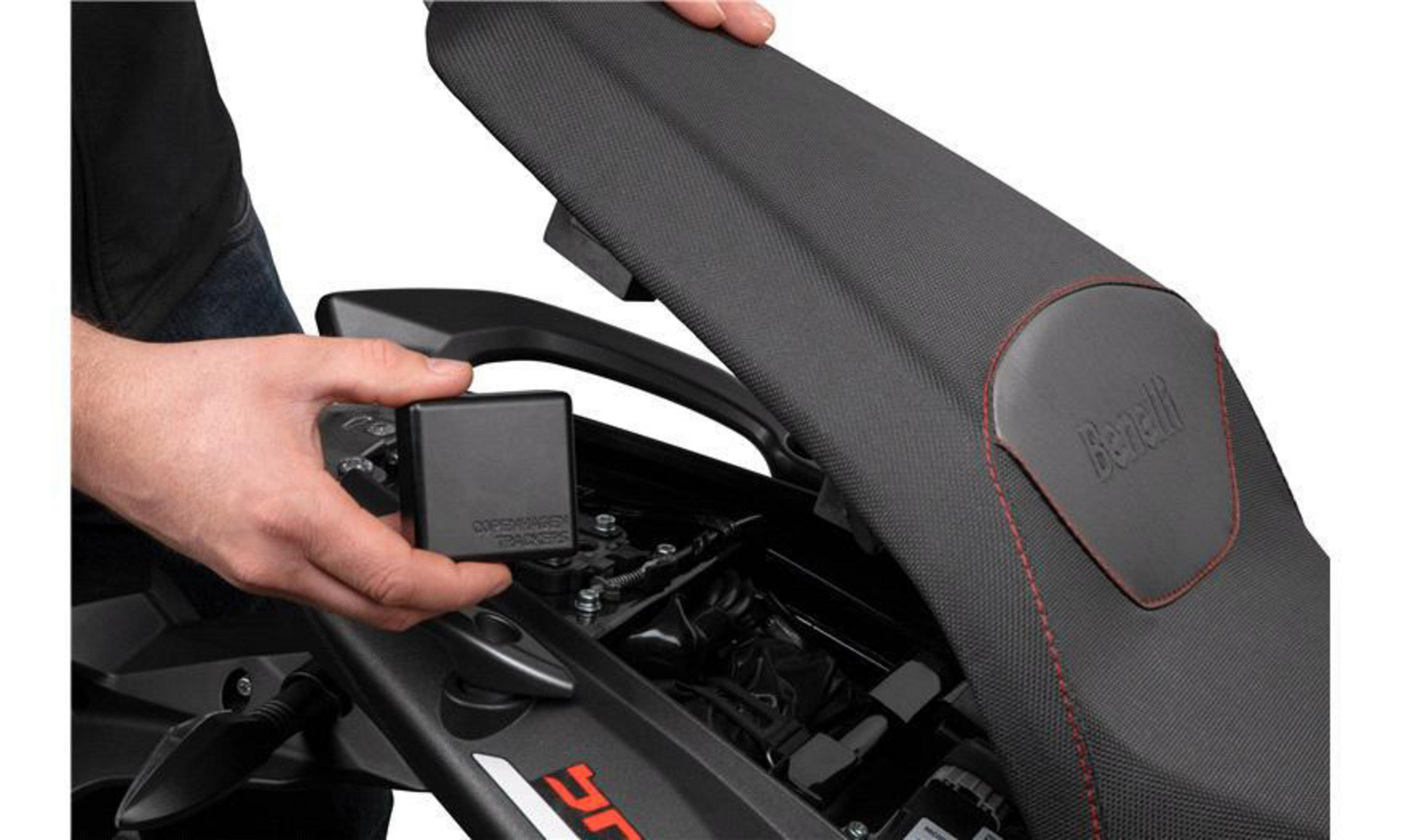 Hände einer Person in der Nähe eines Motorradsitzes, die eine schwarze Box halten, der Sitz ist offen.