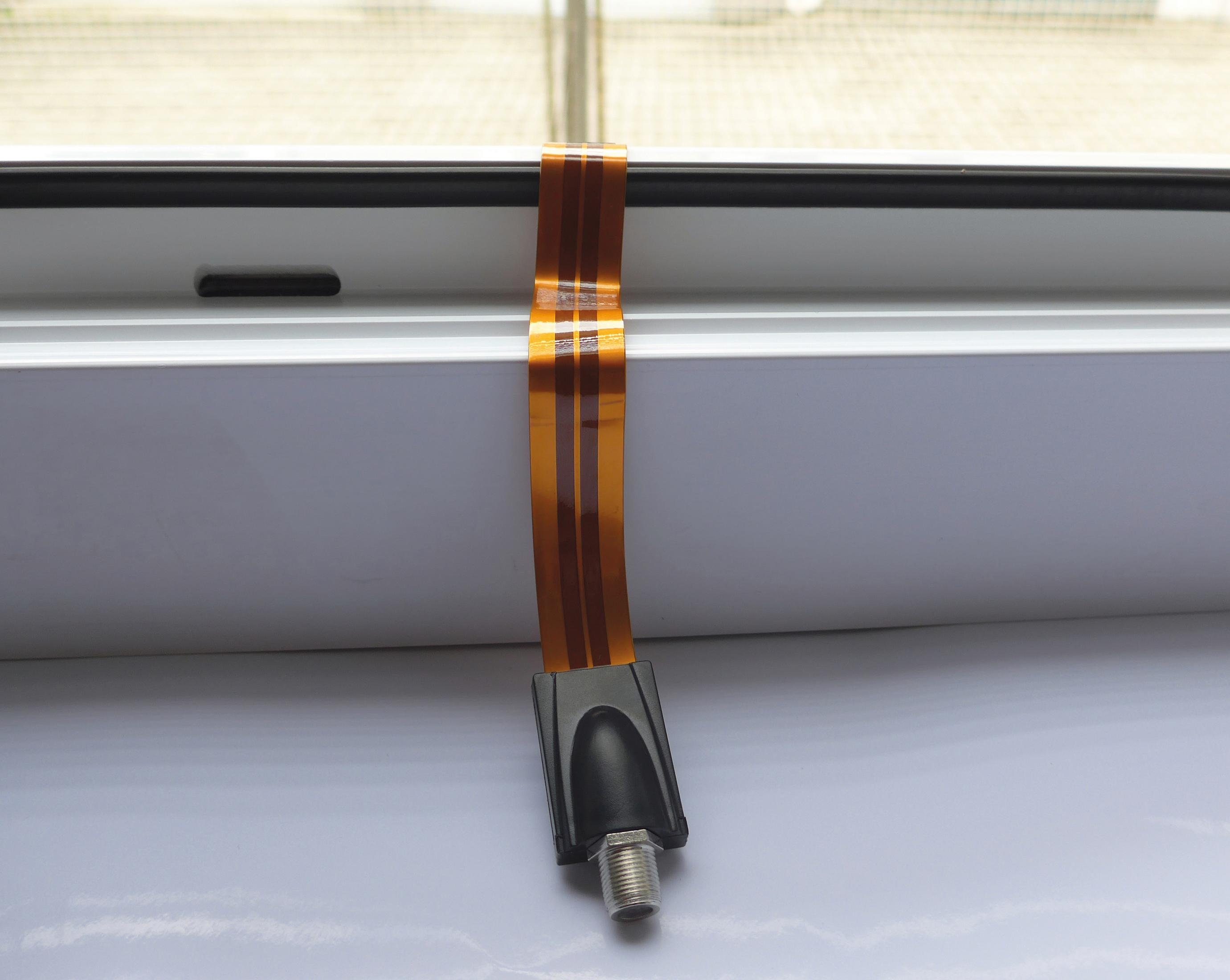 Ein flexibles orangefarbenes Kabel mit einem schwarzen Stecker ist mit einem silberfarbenen Stecker verbunden und liegt auf einer weißen Oberfläche.