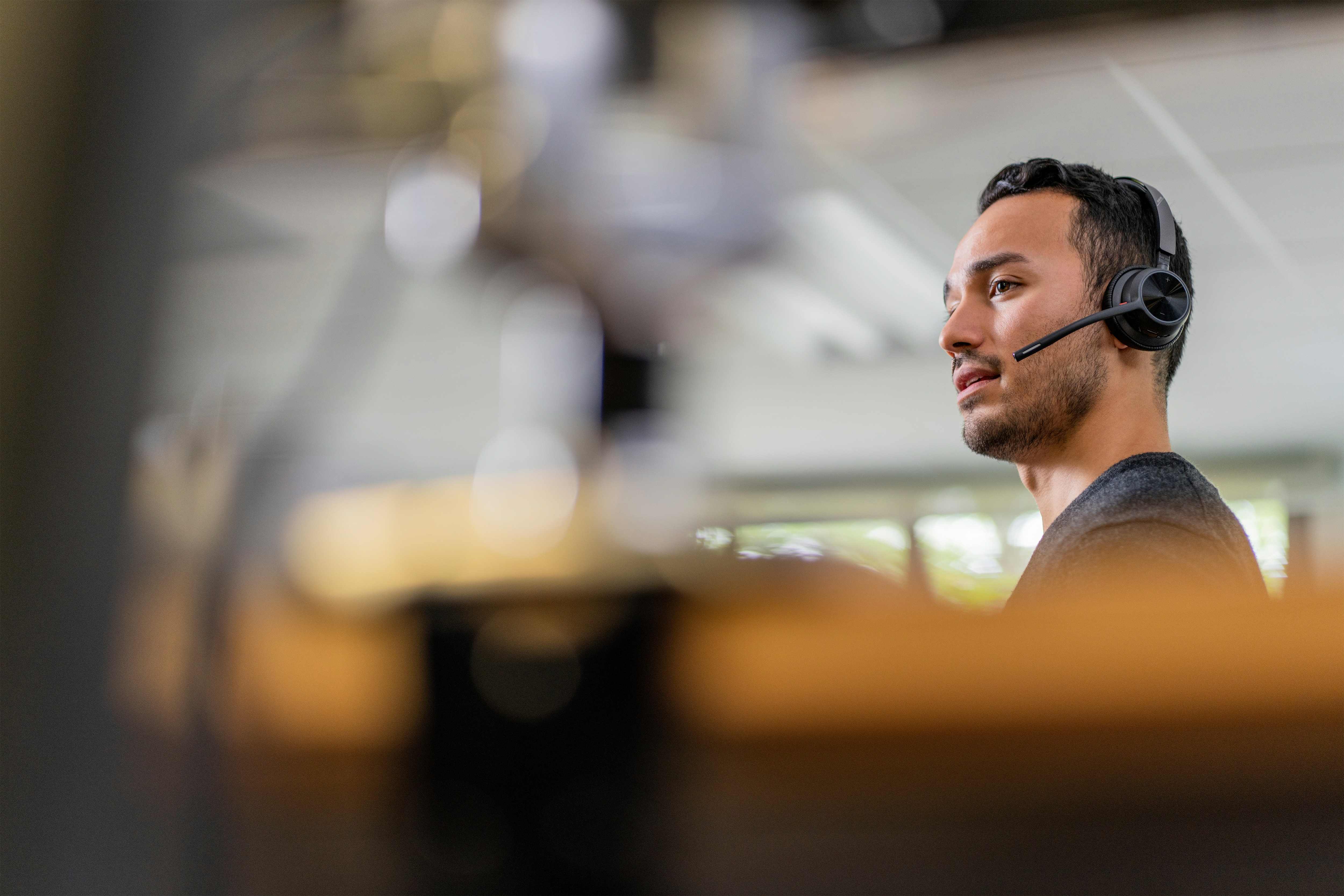 Mężczyzna w zestawie słuchawkowym, patrzący w prawo. Rozmyte tło biura.