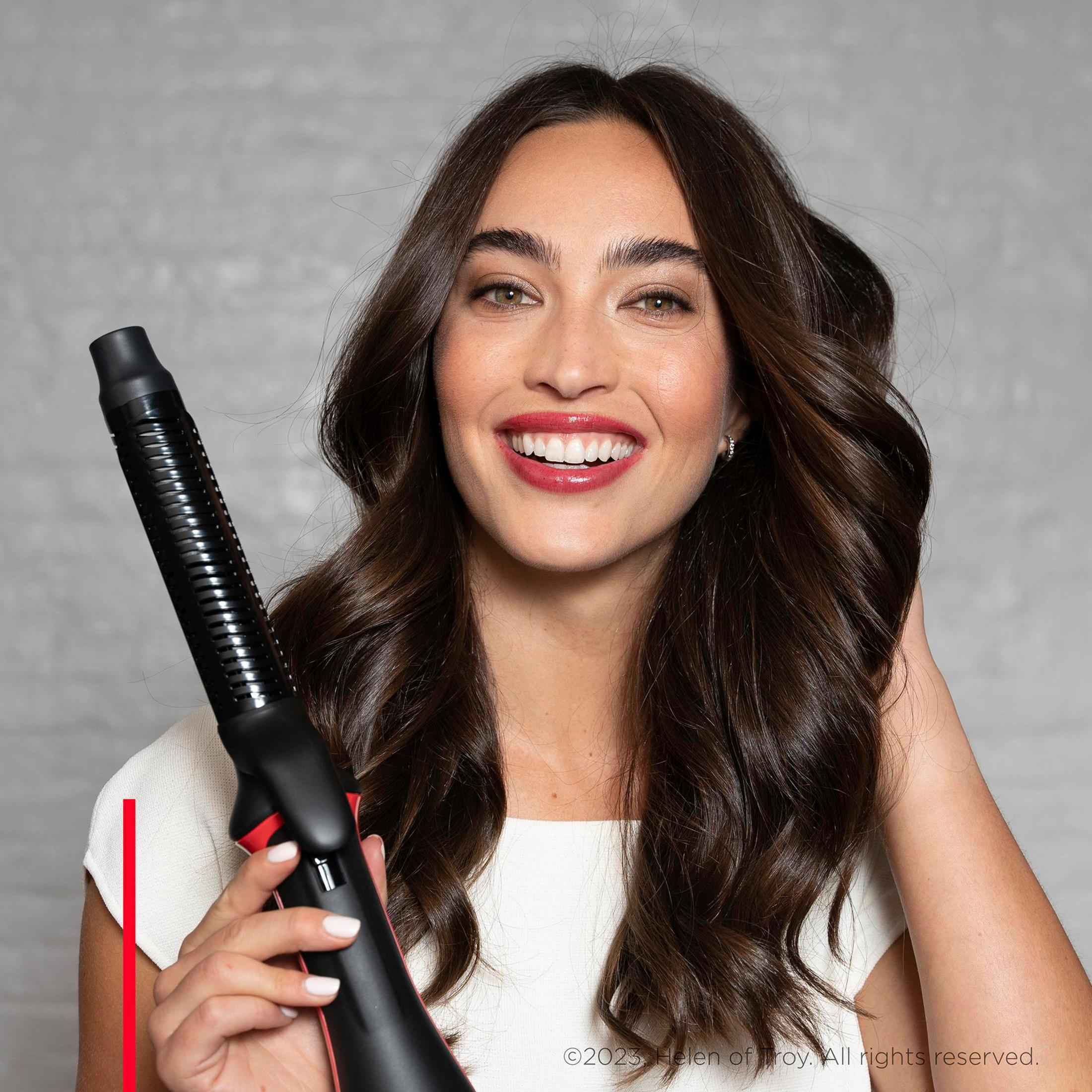 Donna sorride, tiene uno strumento per lo styling dei capelli nero e rosso, capelli acconciati.