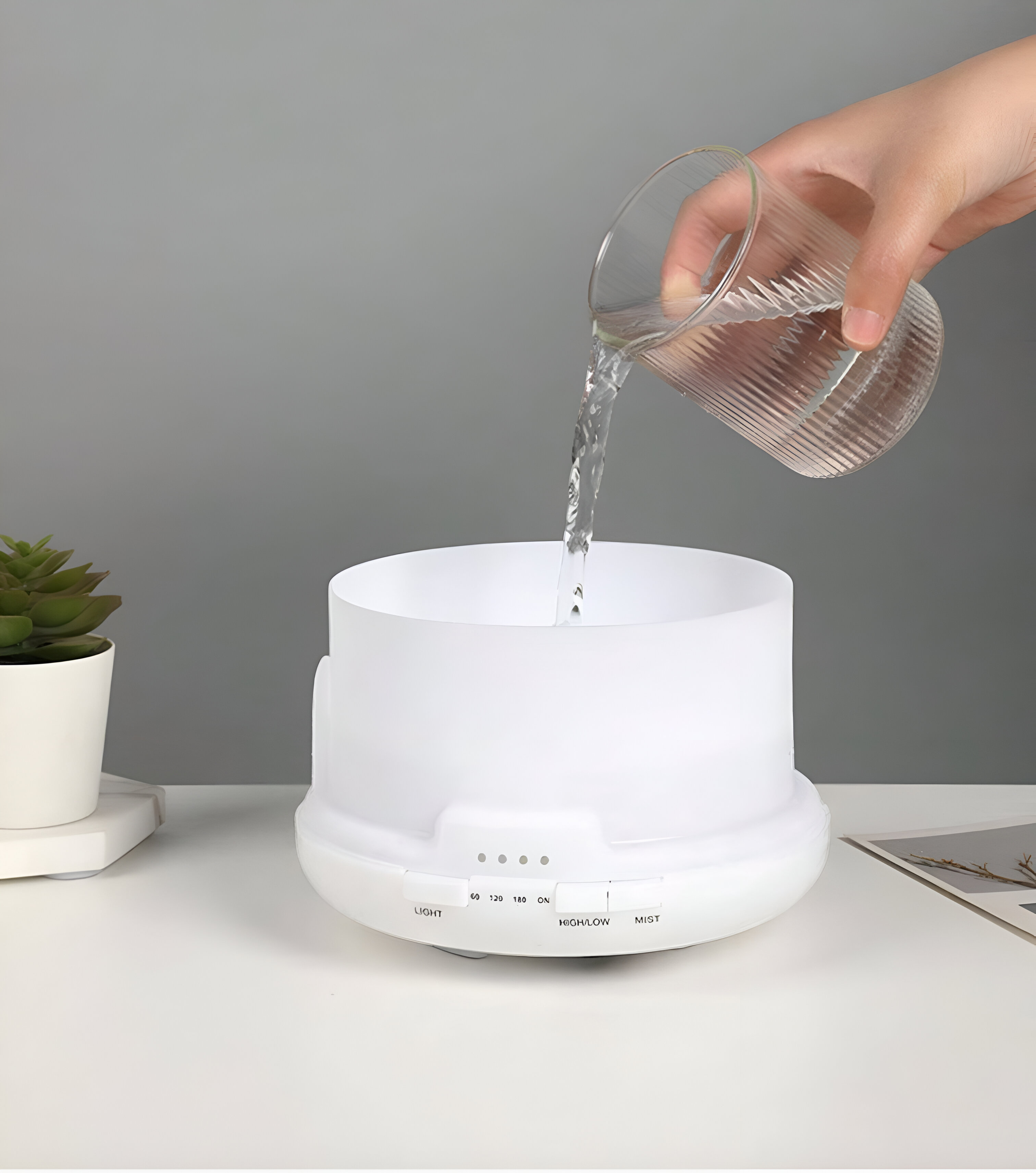 Una persona vierte agua en un difusor blanco. El difusor está sobre una mesa.
