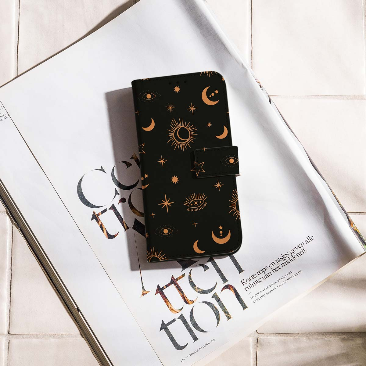 Zwarte telefoonhoes met gouden hemelse ontwerpen op een tijdschrift. De hoes is open, met de binnenkant zichtbaar. Het tijdschrift is open.
