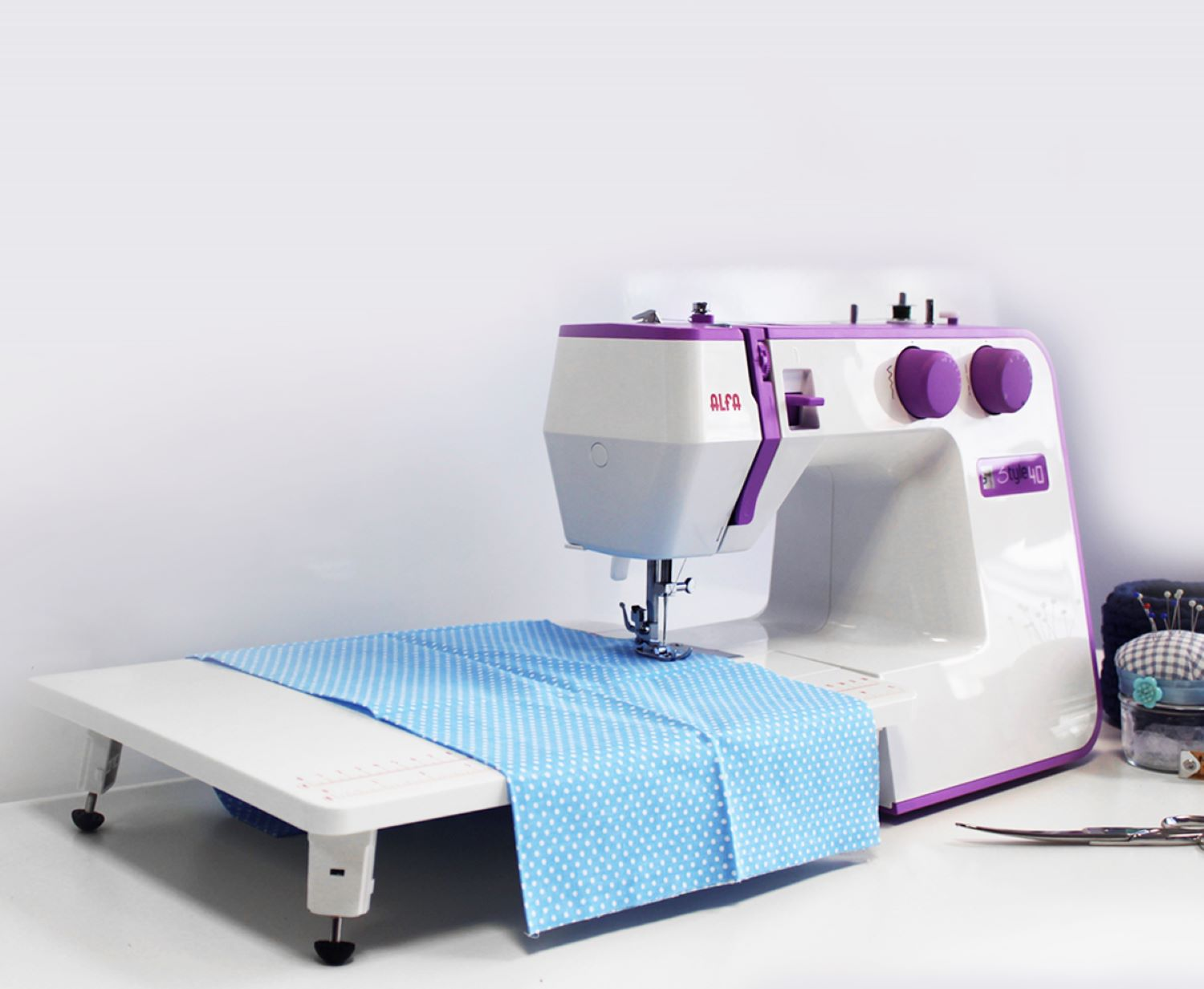 Una máquina de coser Alfa blanca con tela azul sobre una mesa blanca, cosiendo.